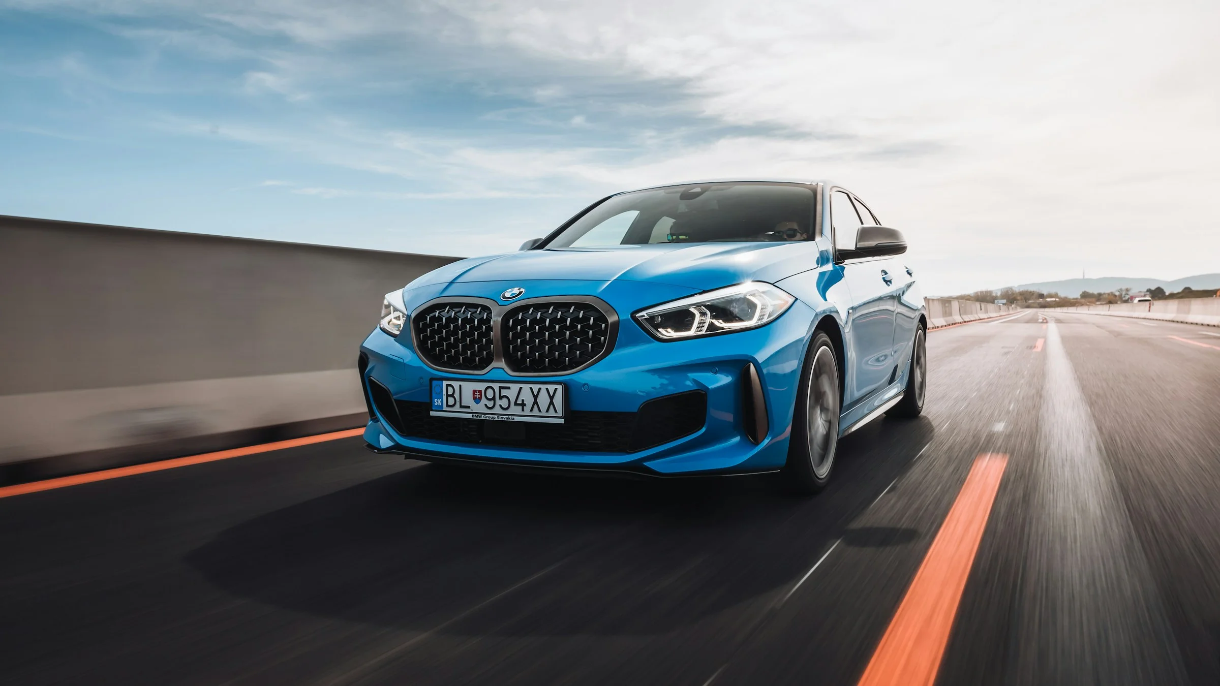 Blue BMW sedan driving on a highway at high speed with motion blur and clear sky background.