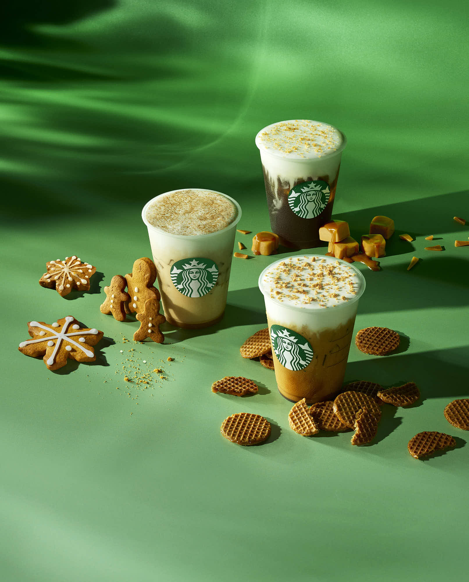 Three Starbucks holiday drinks with festive cookies and caramel on a green background.