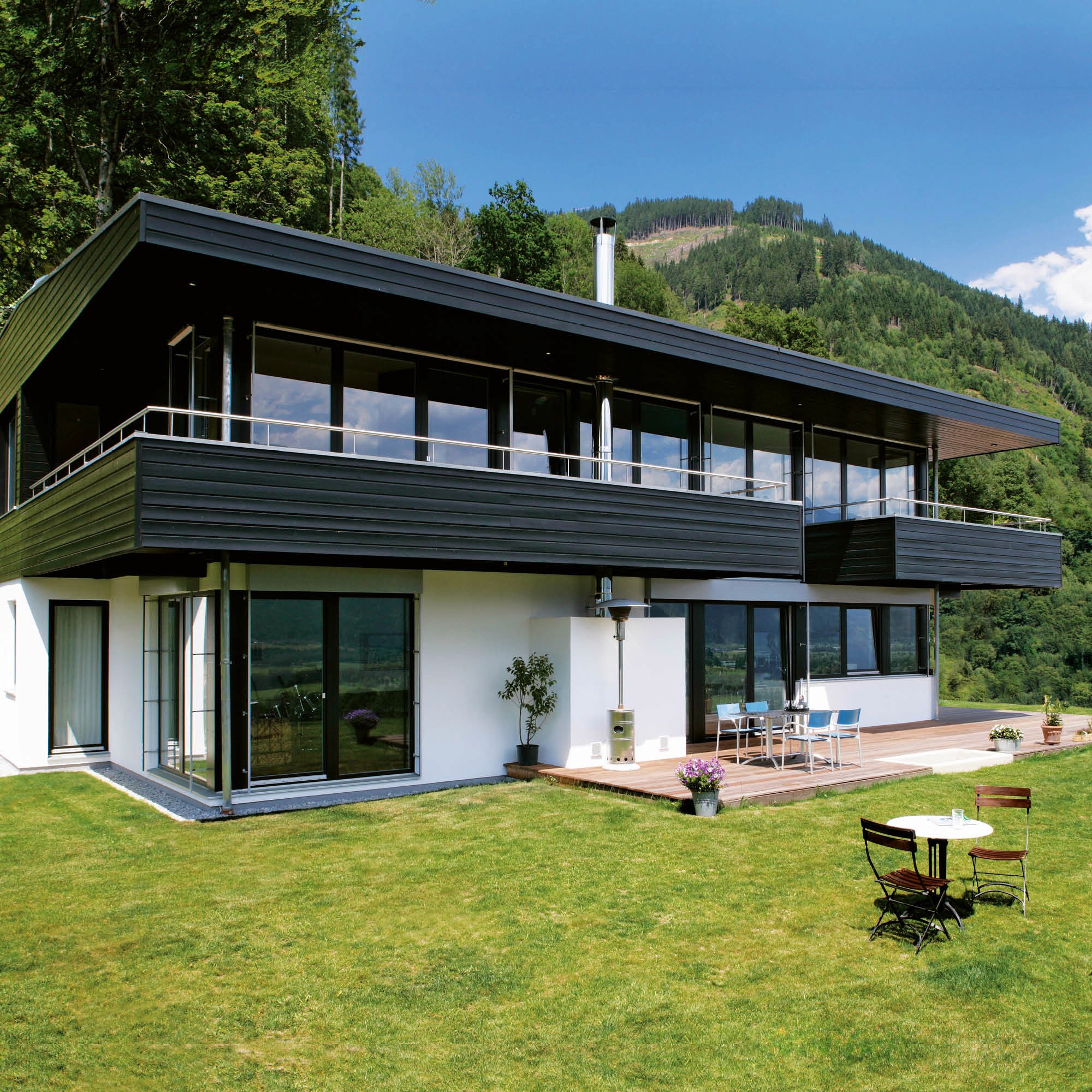Modernes Haus mit breiten Panoramafenstern und schwarzem Giebeldach im Einklang mit der Berglandschaft.