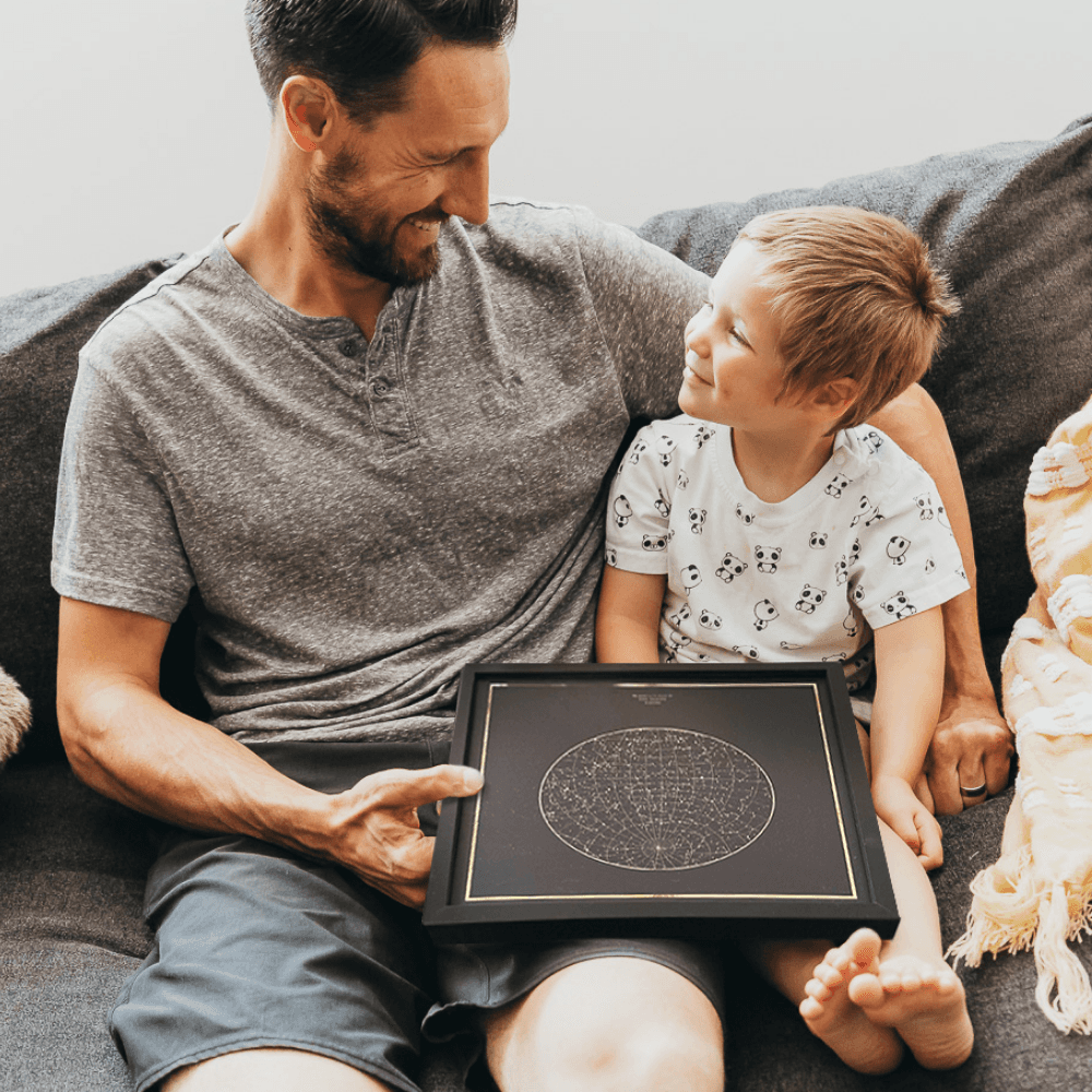 Father and son staring at each other and smiling while holding a Night Sky Star Map print.