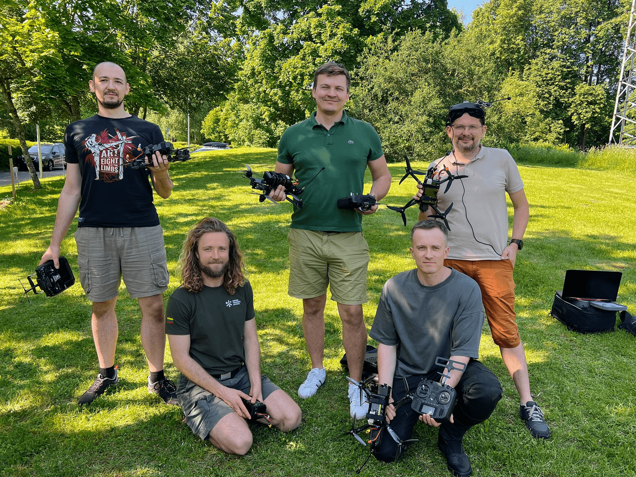 Group of people posing outdoors with drones on the grass