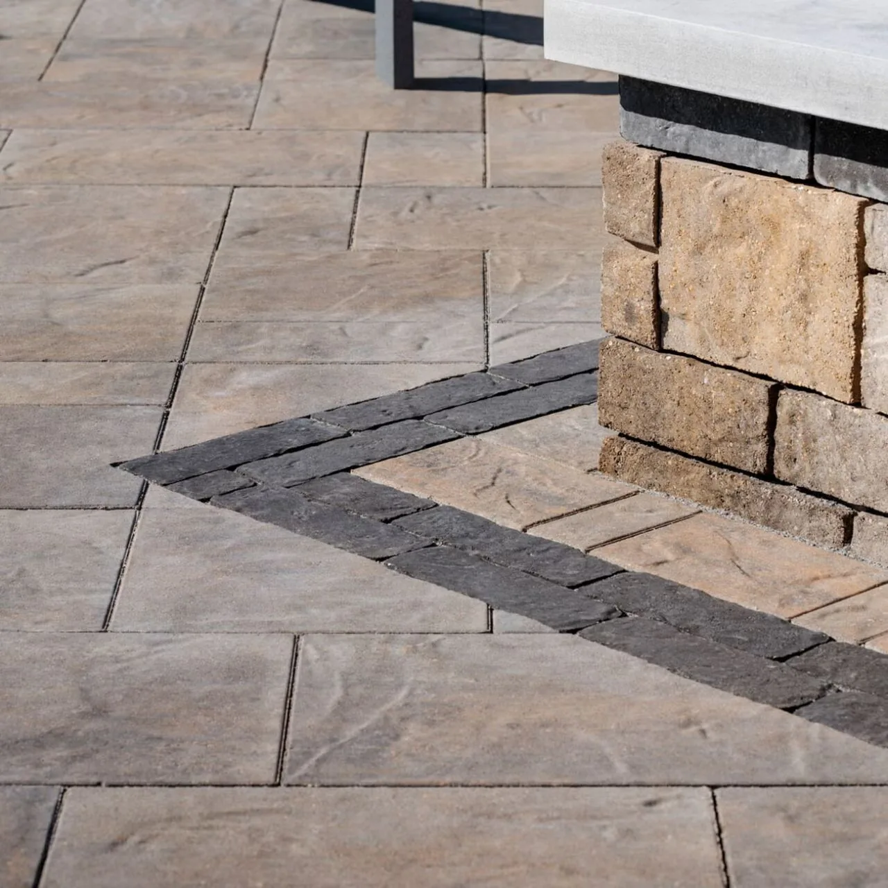 Textured rectangular paving with a dark border beside a stone-clad garden wall.