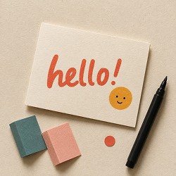 A greeting card reads "hello!" in orange with a smiling face beside it. Below are two erasers, one pink, one teal, and a black marker, on a beige surface.