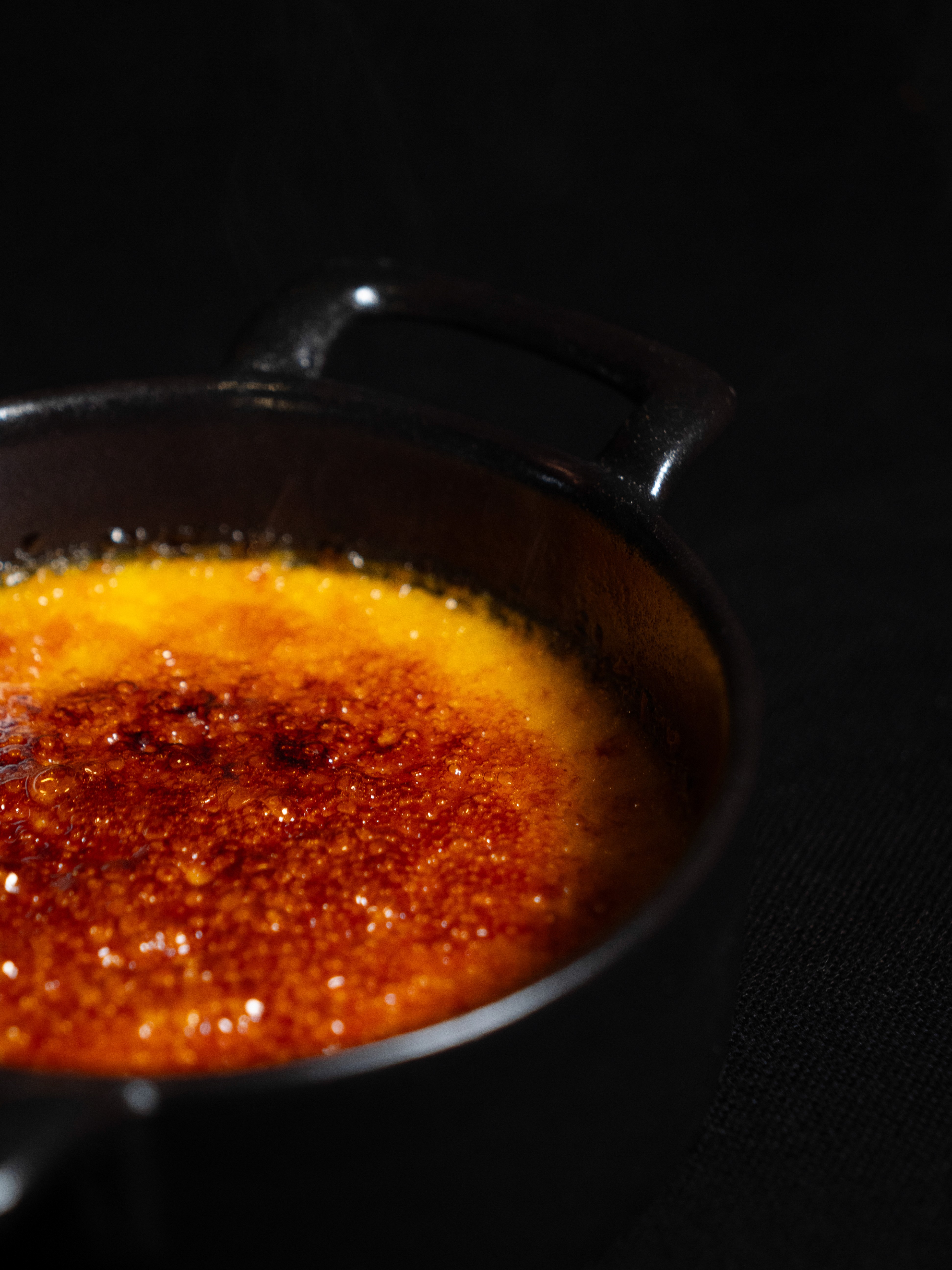 White plate with roasted carrots served on green sauce, topped with almonds and fresh herbs, held by a hand over a dark table.