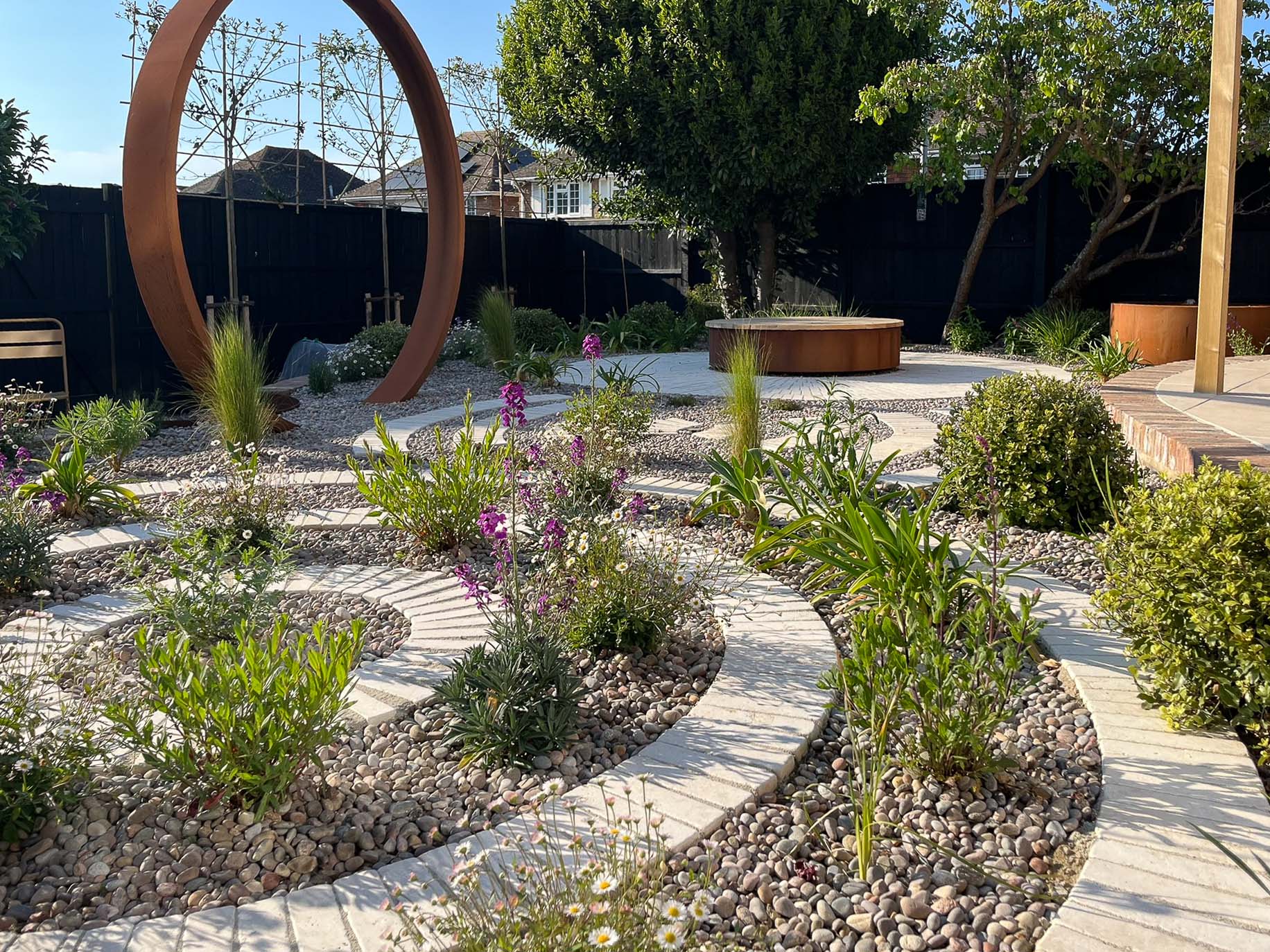 A landscaped garden featuring pathways, circular designs, and greenery, with modern sculptures in the background.