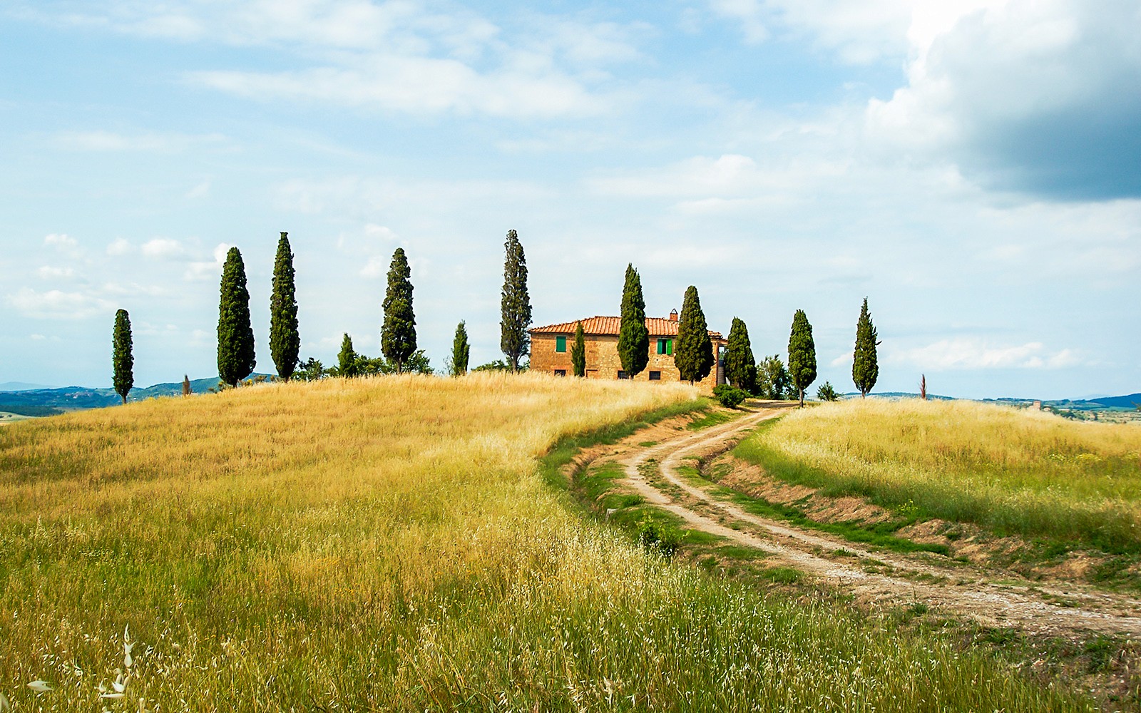 Tuscan countryside with a dirt path leading to a farmhouse near Siena, Italy.