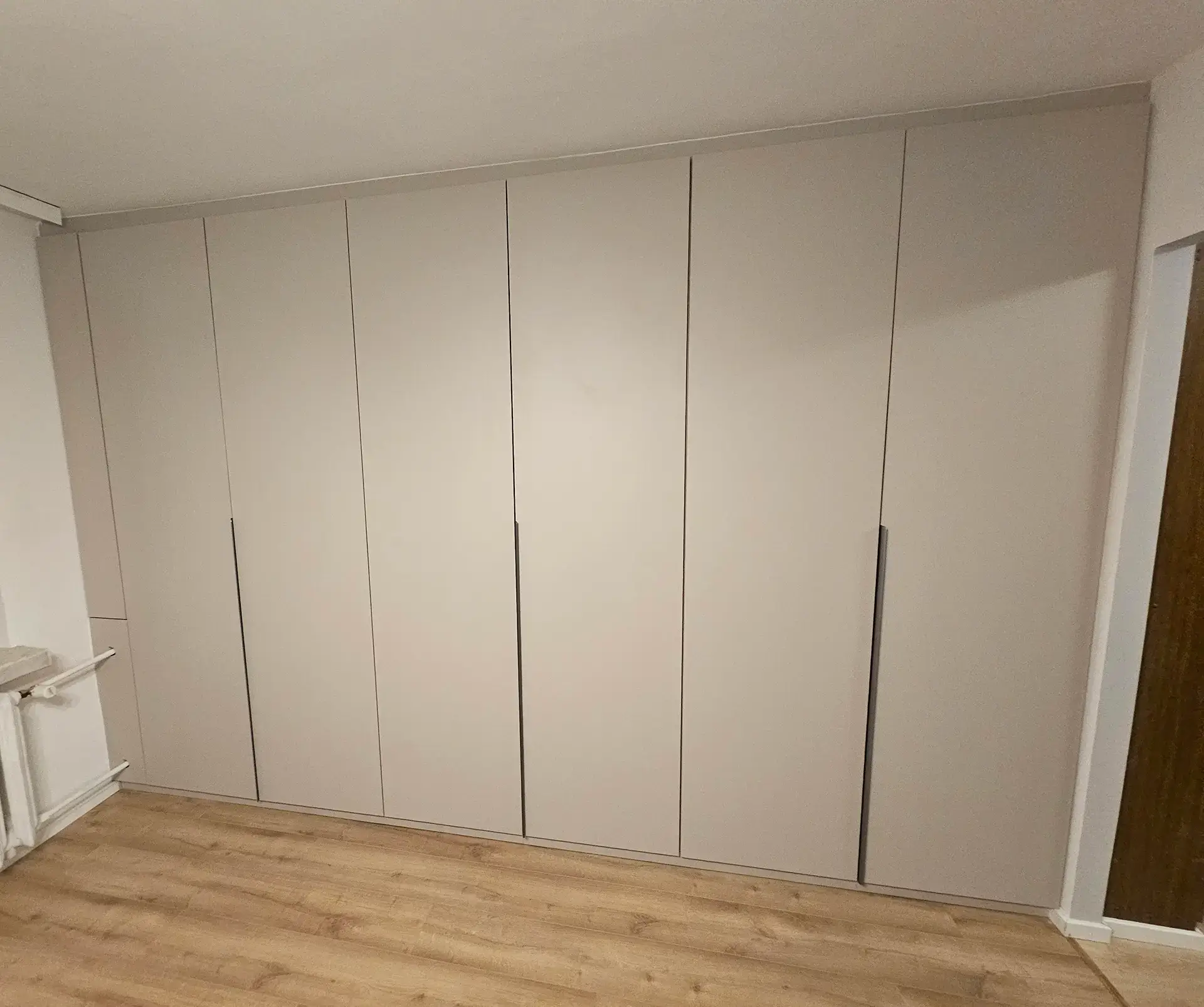 Duża, minimalistyczna szafa biurowa w kolorze jasnoszarym, zabudowana pod sufit.