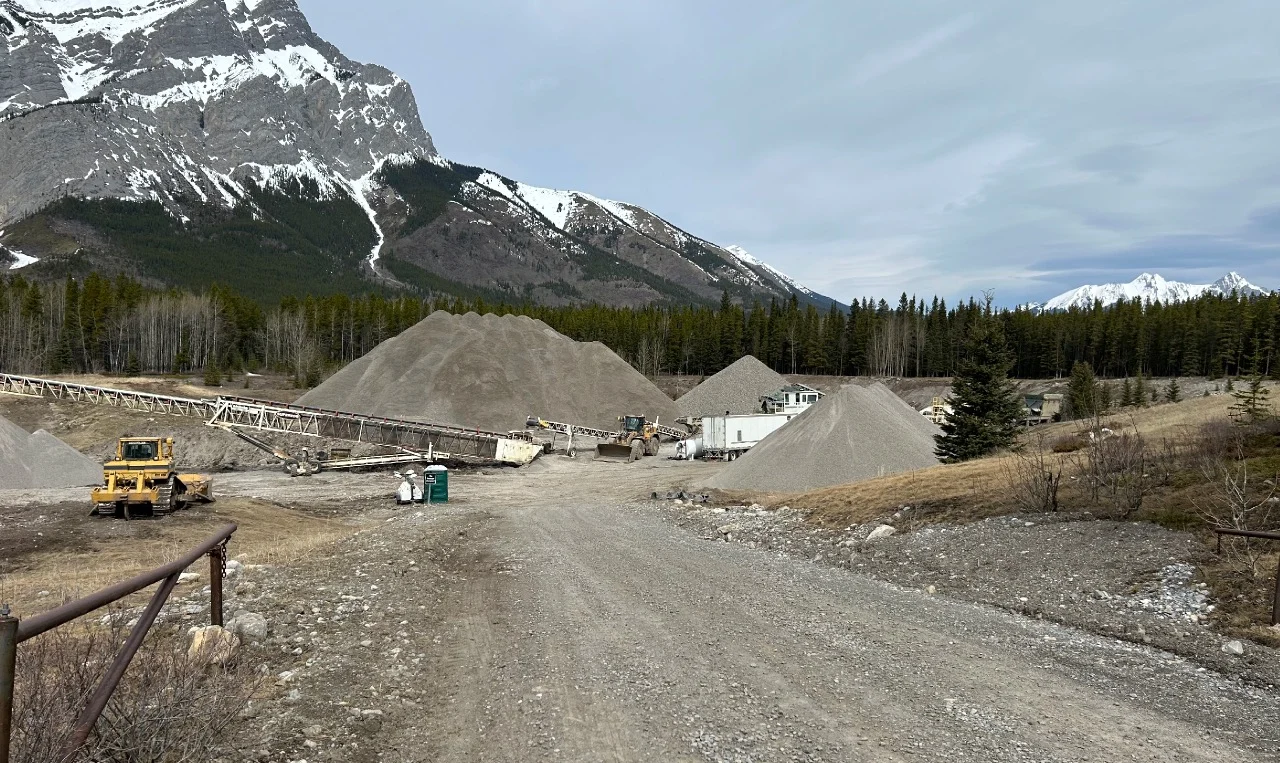 Gravel crushing and stockpiling operation at a Storage Yard in Kananaskis, Alberta, below snow-capped mountains