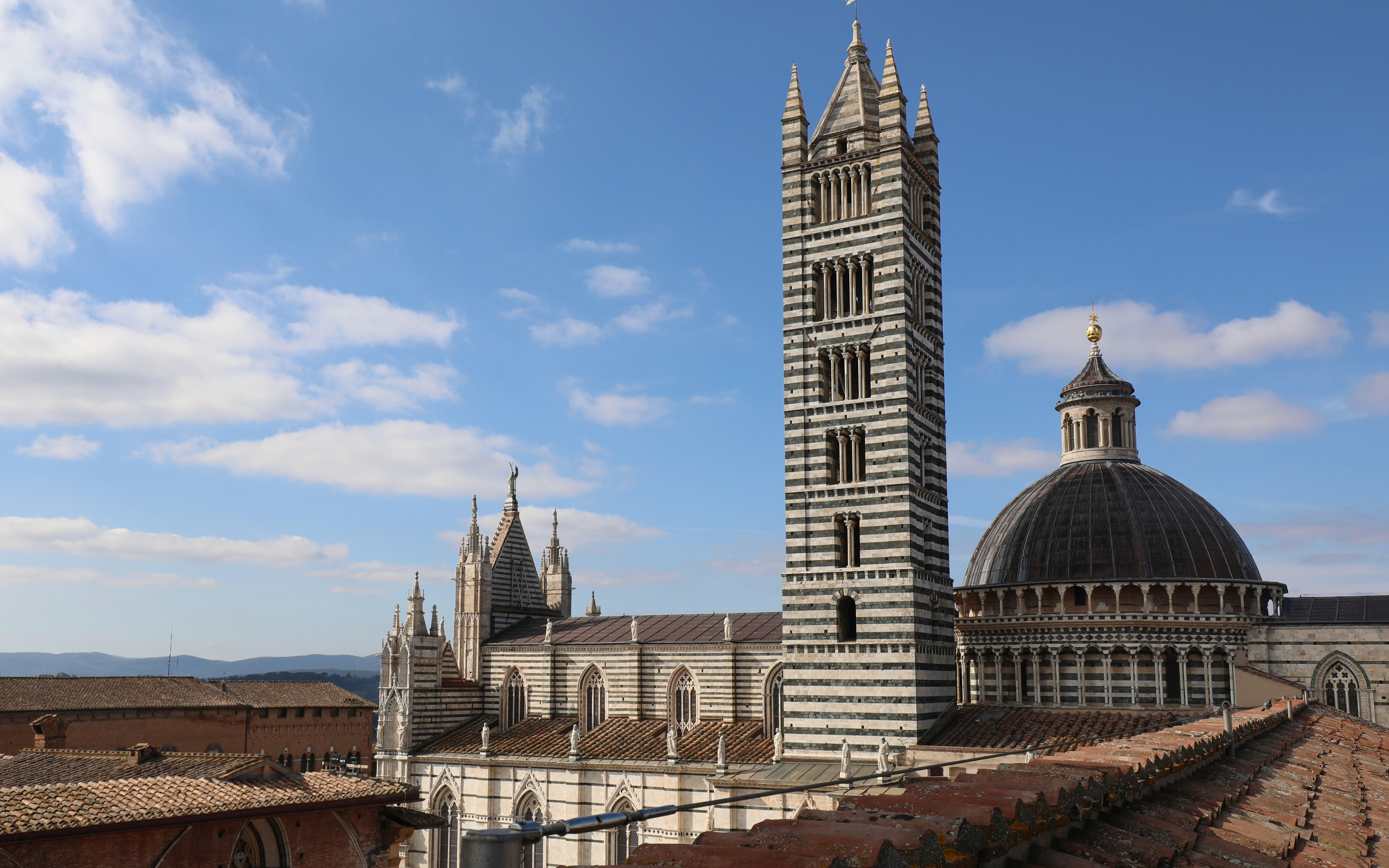 Siena Cathedral Facciatone viewpoint with bell tower and dome under blue sky.