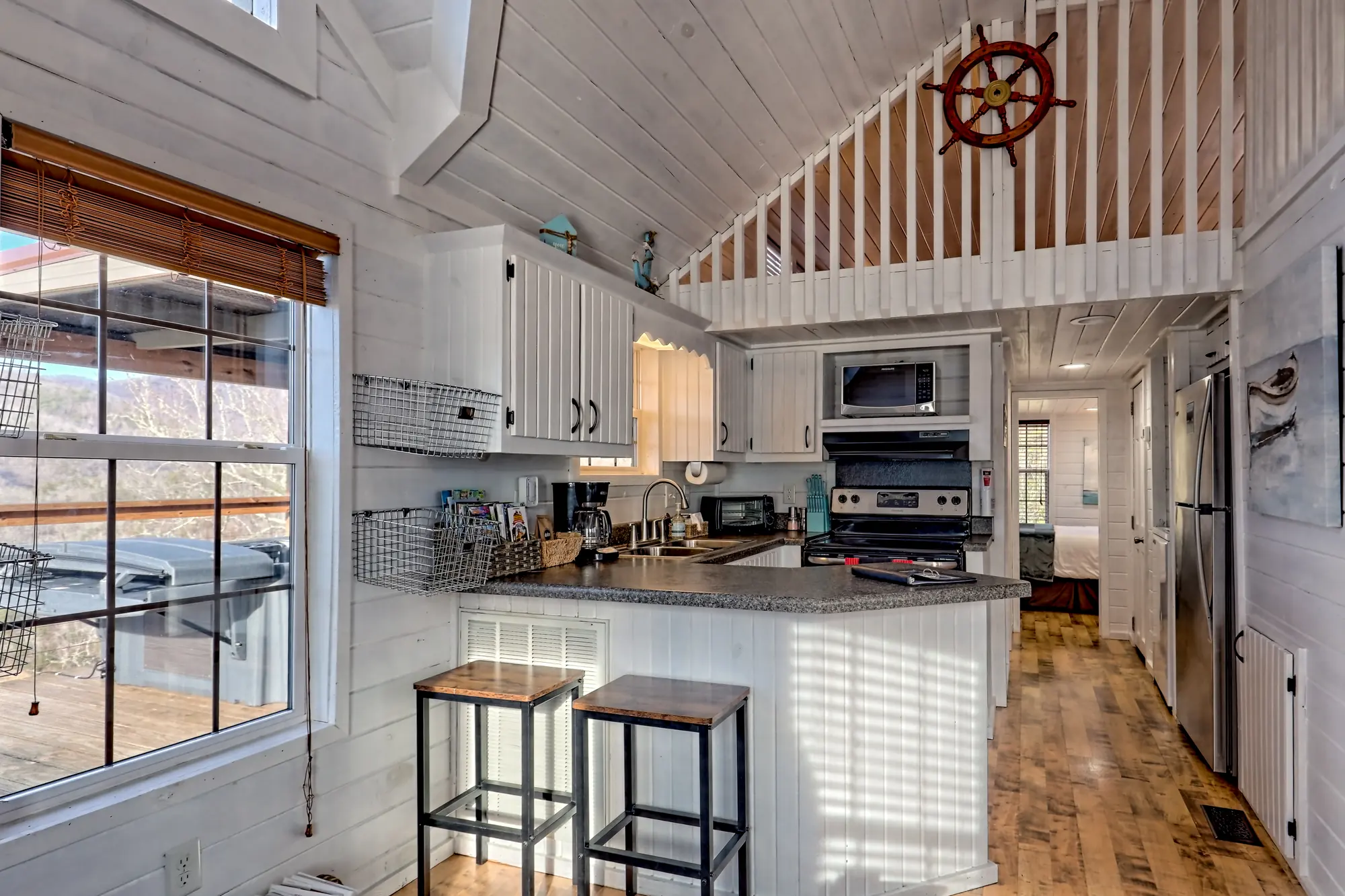 Tiny Tuck kitchen with breakfast bar stools, stainless appliances and a ship-wheel loft rail