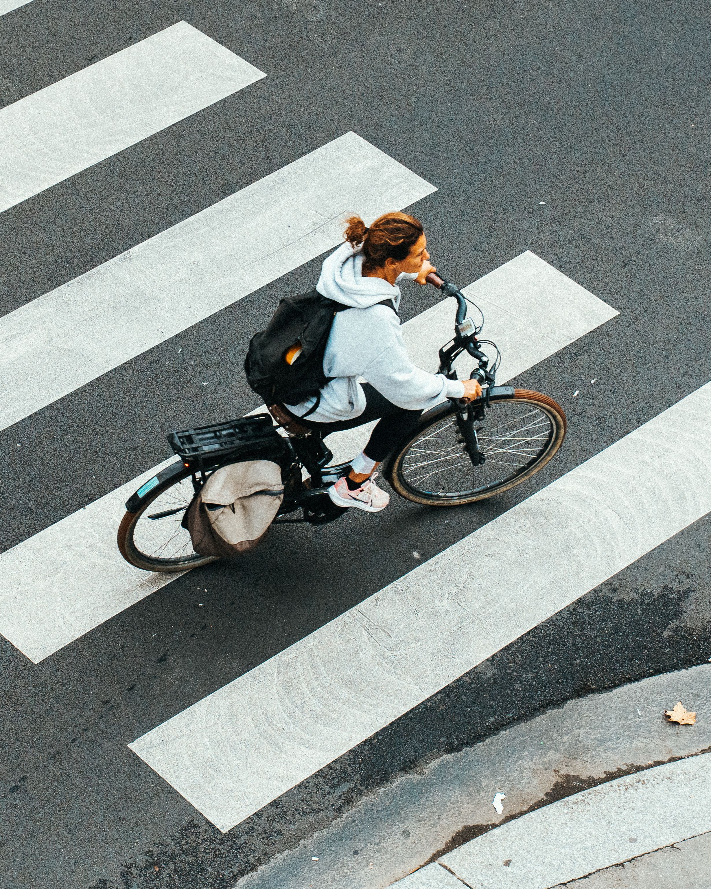 Een fietser steekt een zebrapad over, gefilmd van bovenaf met een gestreept wegdek eronder.