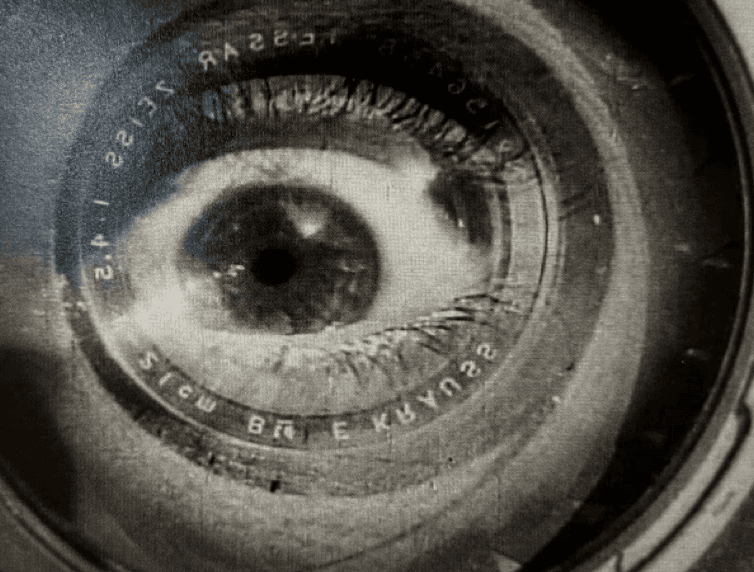 A black-and-white image of a close-up eye inside a camera lens