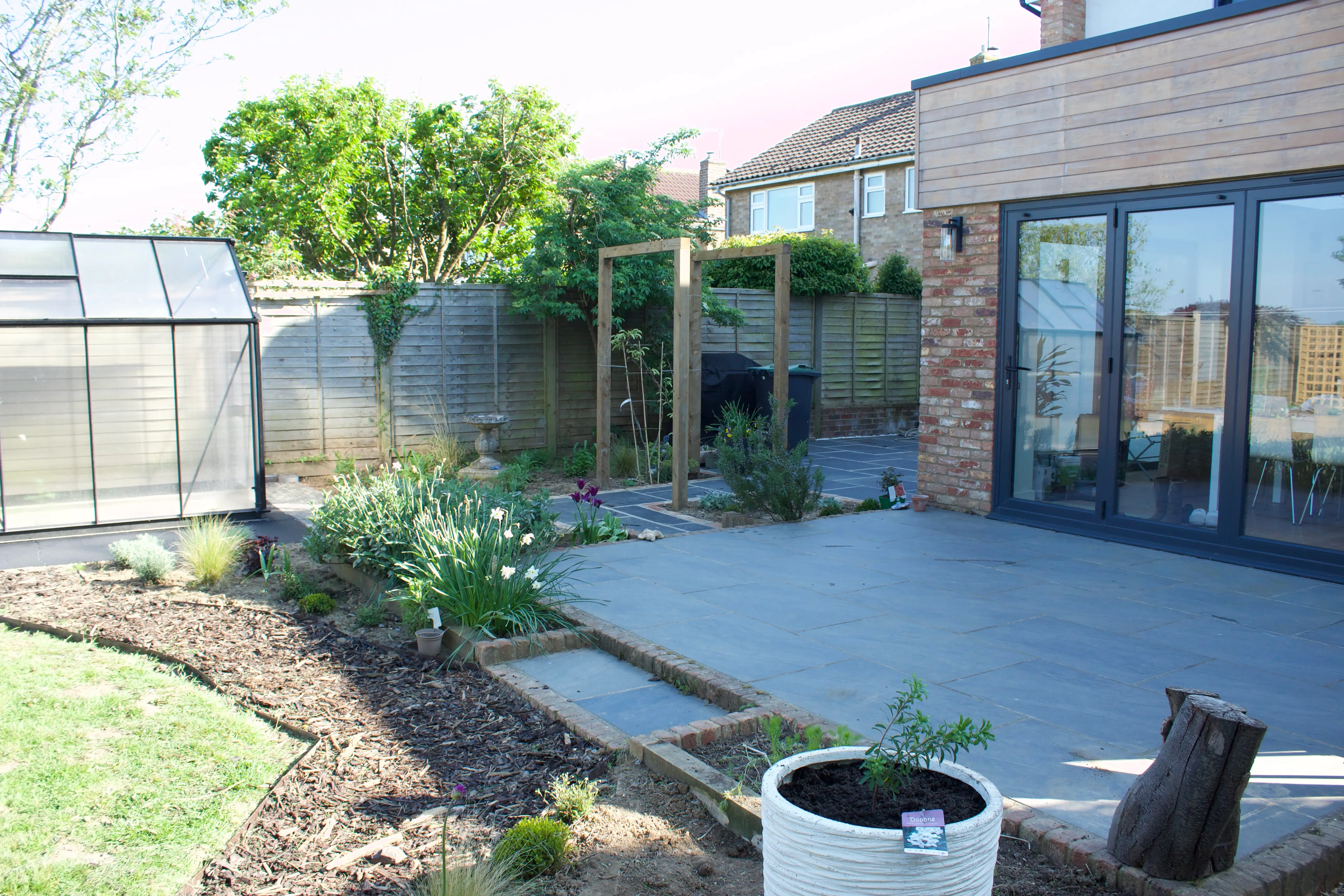 A modern patio area with greenery, featuring a seating arrangement and a well-maintained lawn.