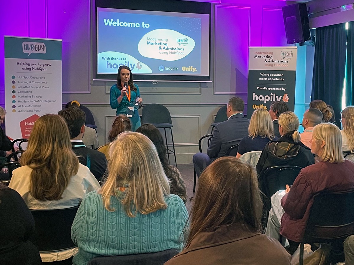 A presenter speaking on stage at HubGem LIVE! event at Exhibit, Balham, welcoming attendees to a session on Modernising Marketing and Admissions using HubSpot, sponsored by Hapily, Unify and Insycle