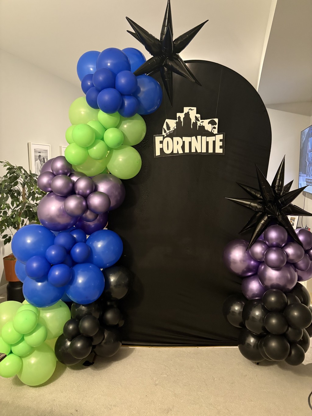 Balloon arch with big 15 inch balloons and 7 inch ballloons in the colours black, purple and blue. The arch is black and has happy birthday sign. The theme is based out of fortnite video game.