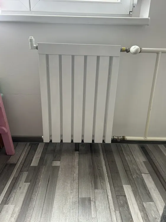 Fehér radiátor új padlóburkolat előtt egy lakásban