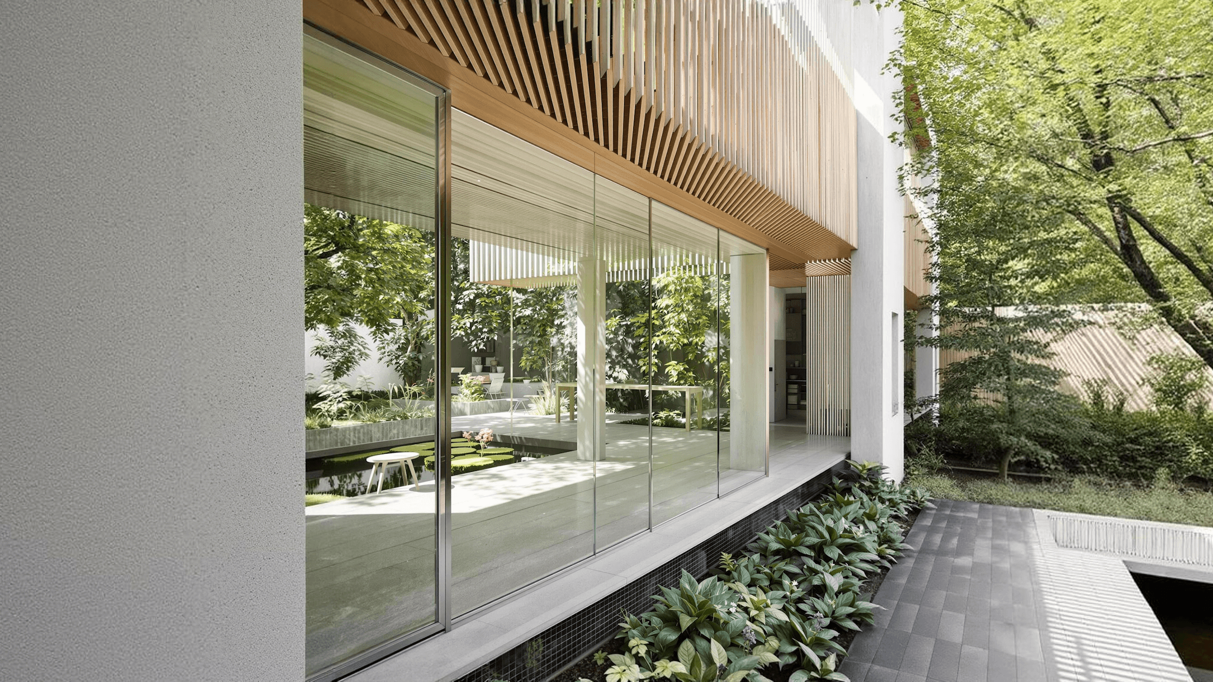 Modern building exterior with large windows, surrounded by greenery and a stone pathway. Natural light filtering through.