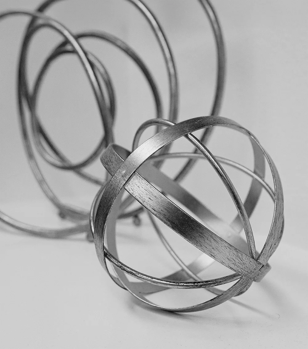 Abstract metallic ribbon sculpture with flowing circular shapes and soft monochromatic tones used as a modern decorative background element.