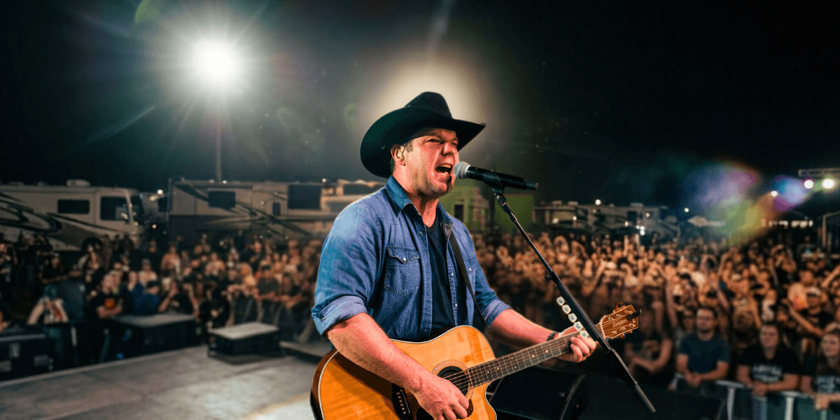 A country music singer performing on stage with a guitar in front of a crowd.