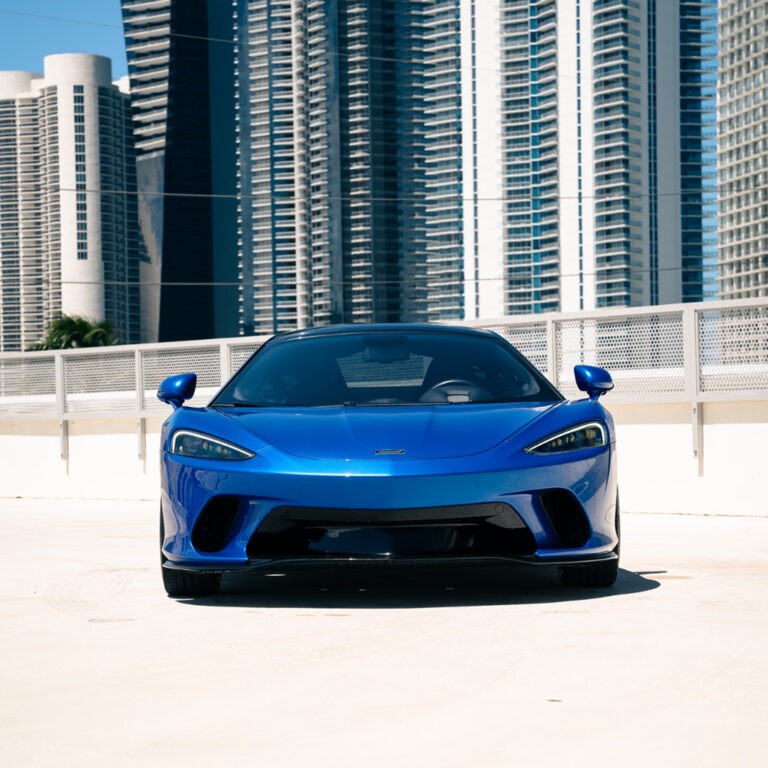 Head-on front view of a blue McLaren GT, displaying its distinctive headlights and aggressive stance.