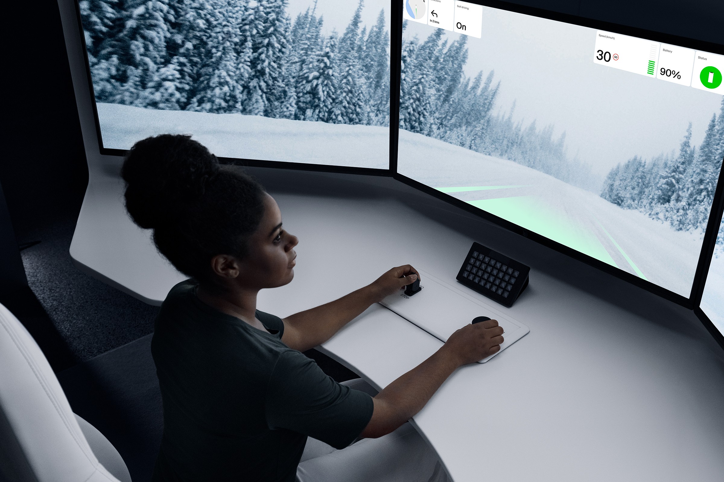 A topdown view of a remote operator at a station desk with three screens and controls.