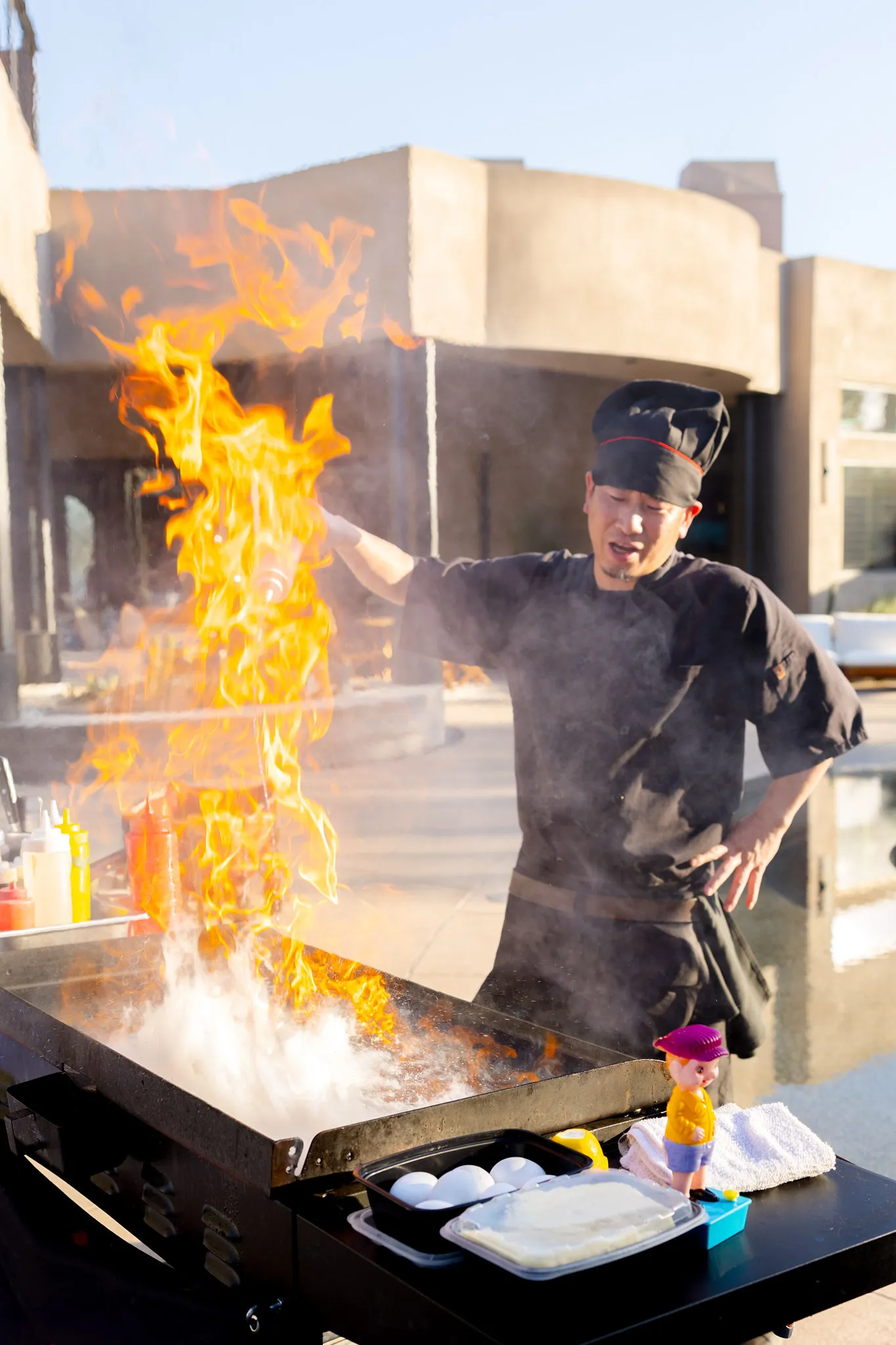 An overhead, rustic photo of a wooden table covered with food, featuring a round pizza cut into quarters, a bowl of French fries, a dish of white cheese slices, and several glasses of water.