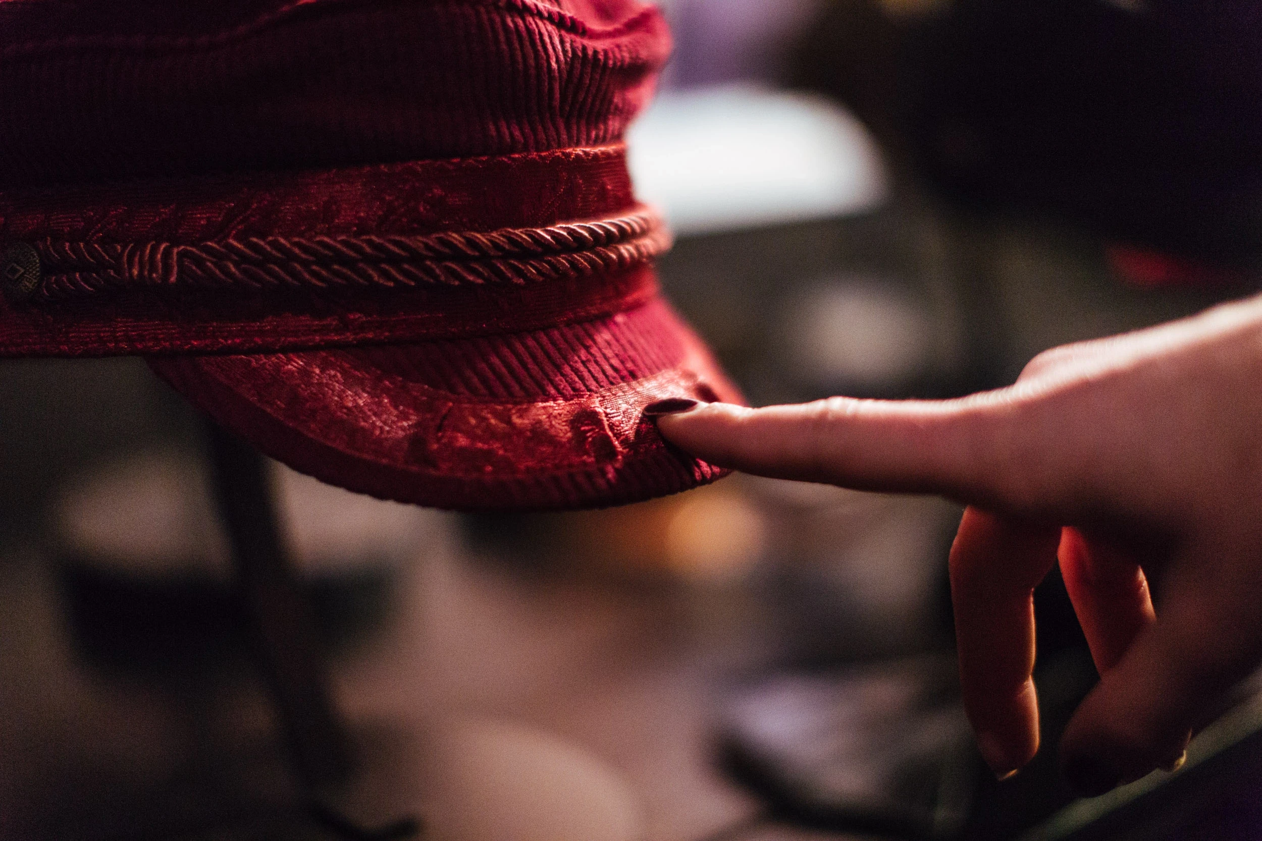 Close-up of a finger touching a red corduroy fiddler cap with rope detail at the BRIXTON pop-up.
