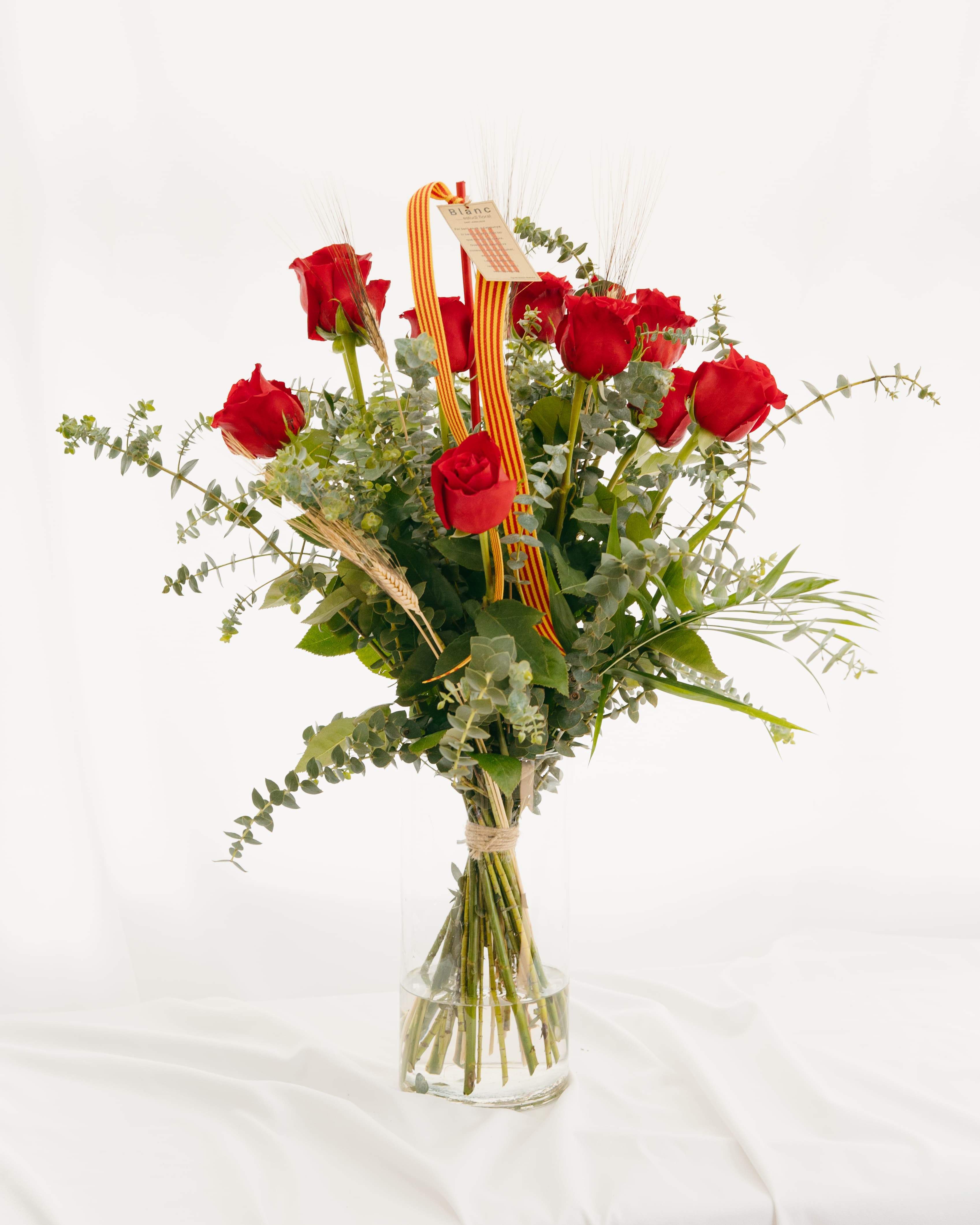 Ram de 12 roses vermelles de Sant Jordi amb eucaliptus, espigues i cinta de la senyera en gerro de vidre, creat per Blanc Estudi Floral.