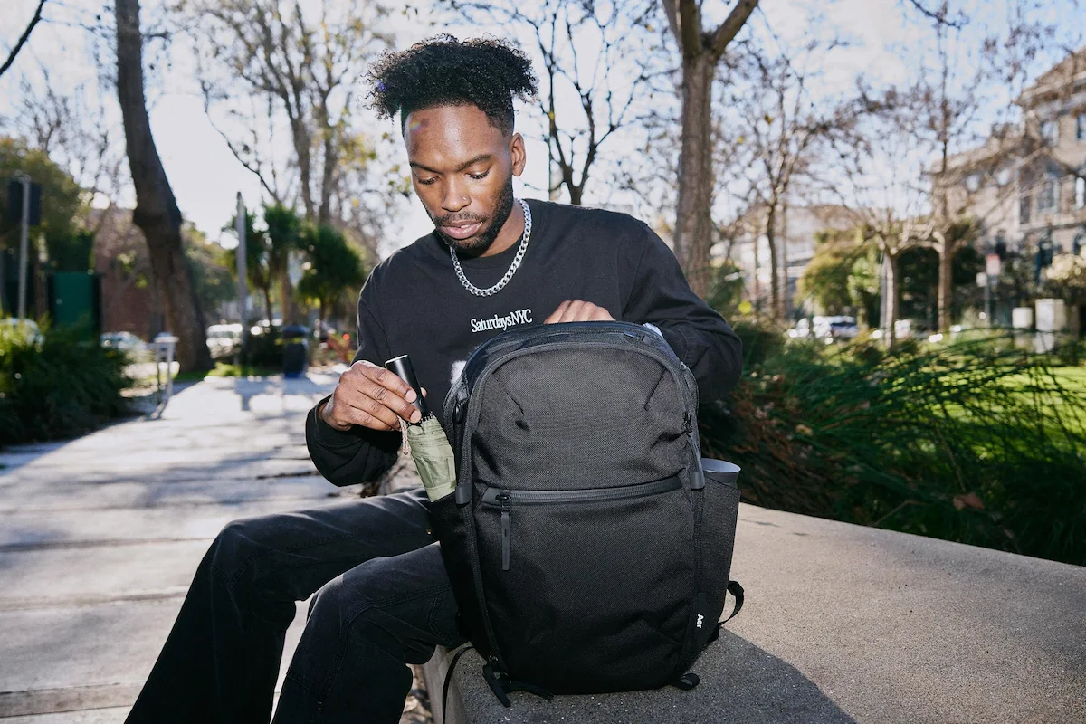 Man opening black backpack sitting on grey park bench