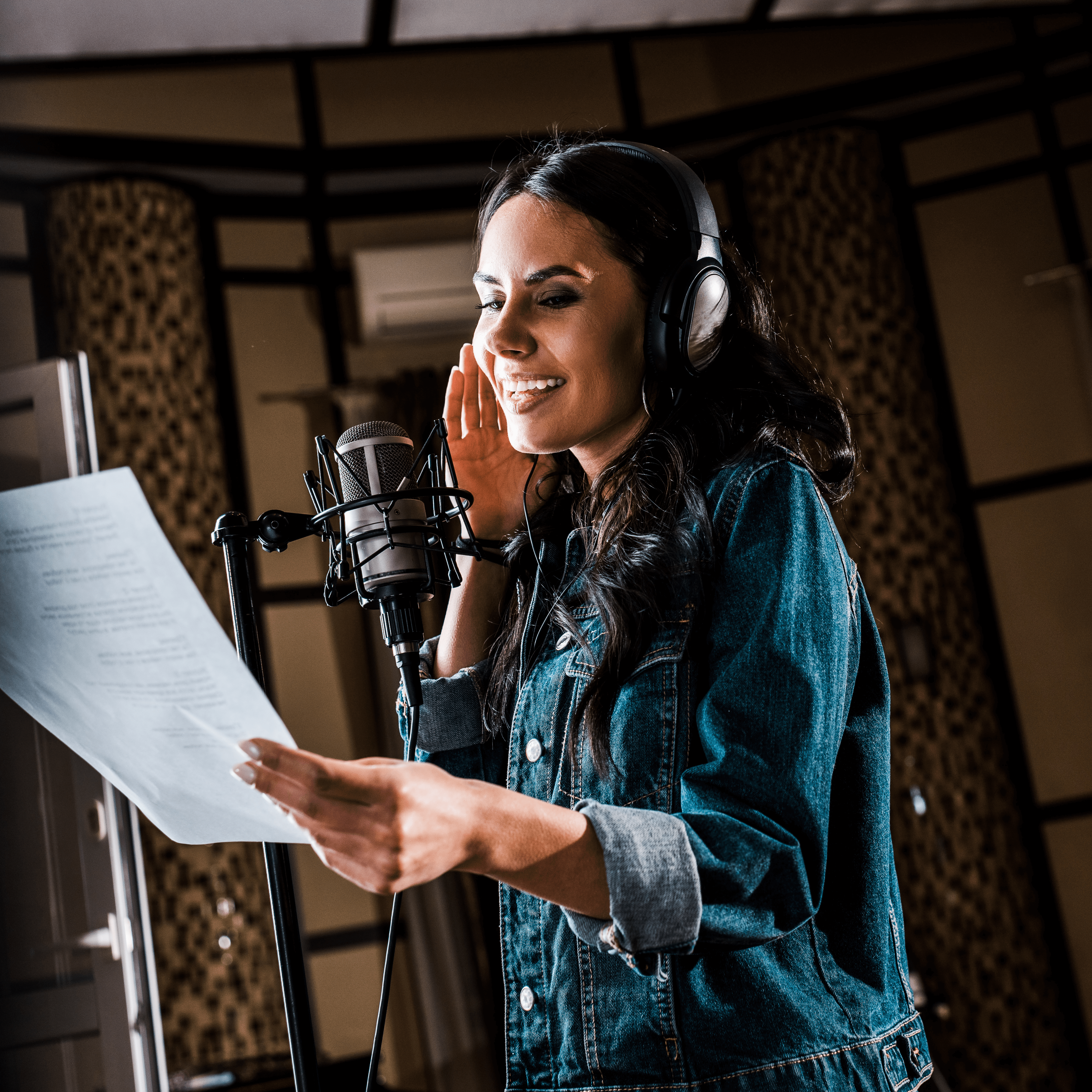 Voice actor recording lines in a studio with a microphone, headphones, and script in hand.