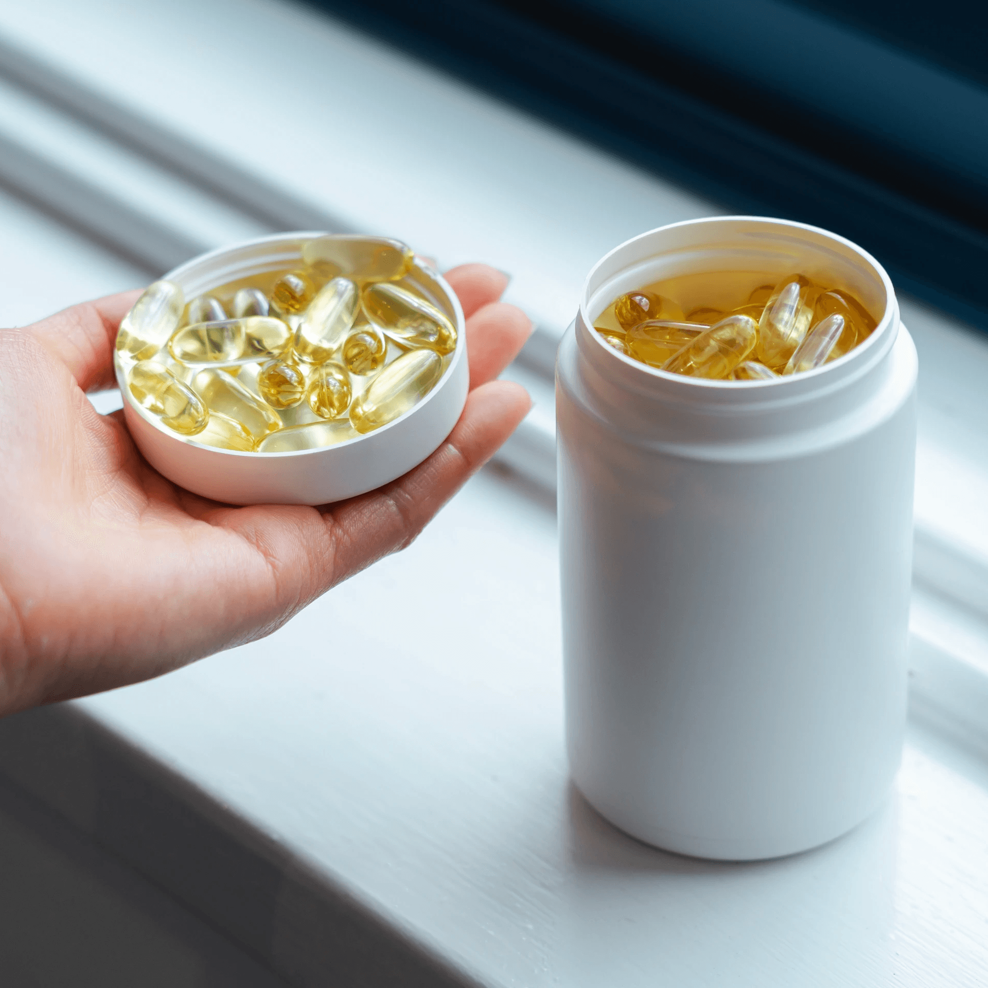 A model holding the open lid of a VIVOMER supplement bottle filled with omega-3 capsules. This highlights the robust seal integrity and food-safe nature of Shellworks' home-compostable packaging.