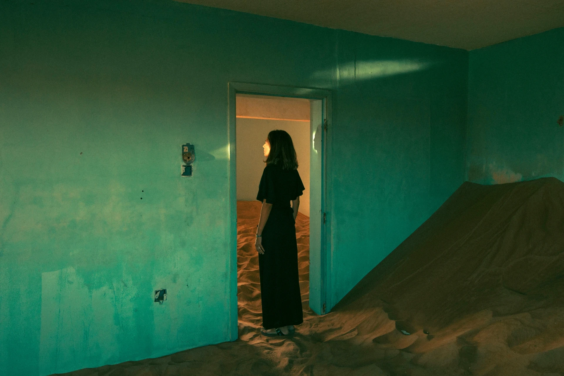 Person steht in einem offenen Türrahmen zwischen kühlem Innenraum und sandgefülltem Raum – Sinnbild für Übergang, Exploration und Experience Design.