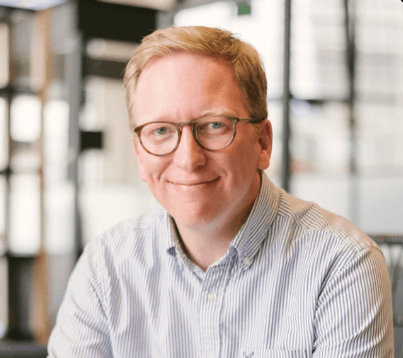 A man with straight blonde hair wearing a light colored shirt.