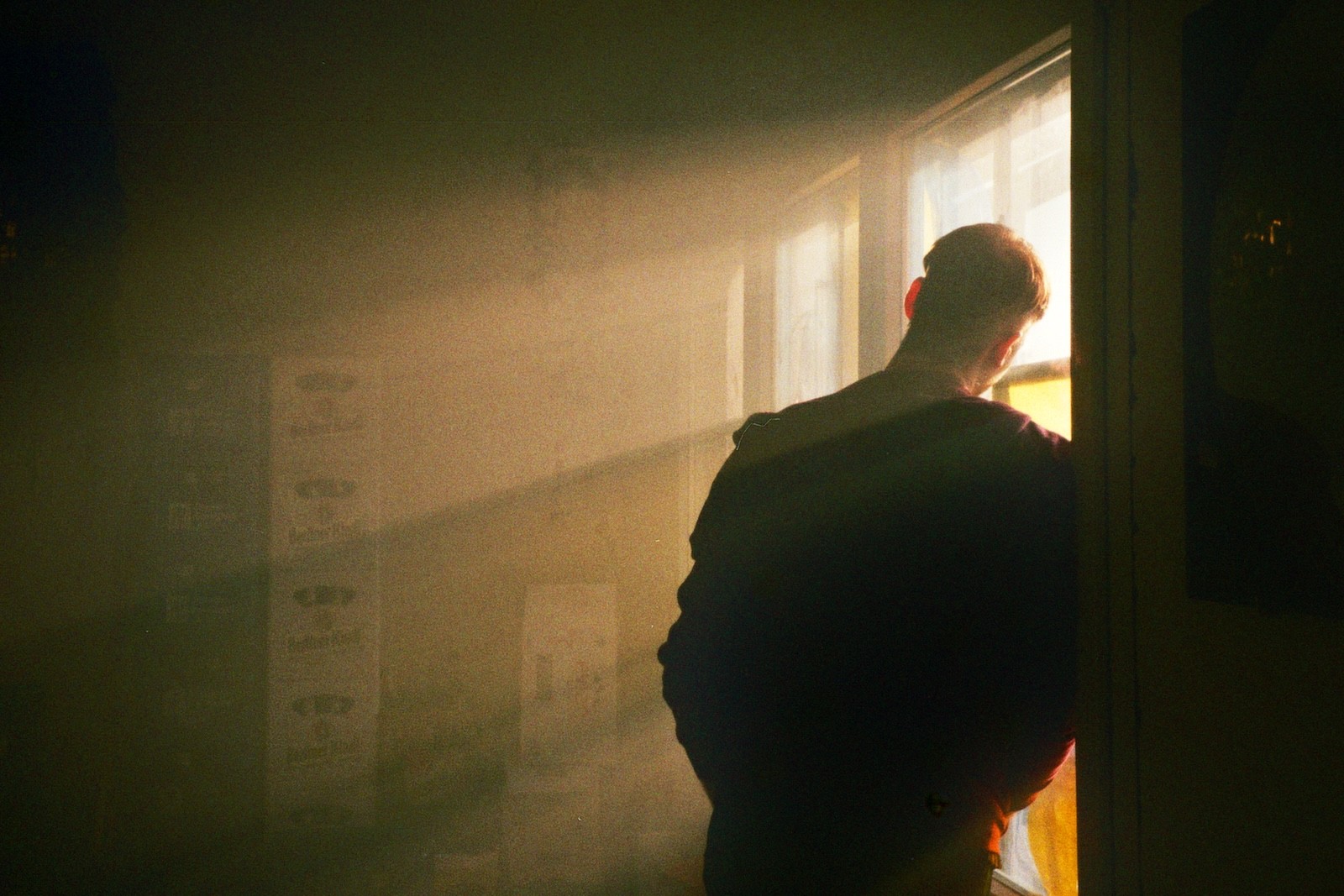 Back view silhouette of a young person looking out a window at sunrise in analog photography