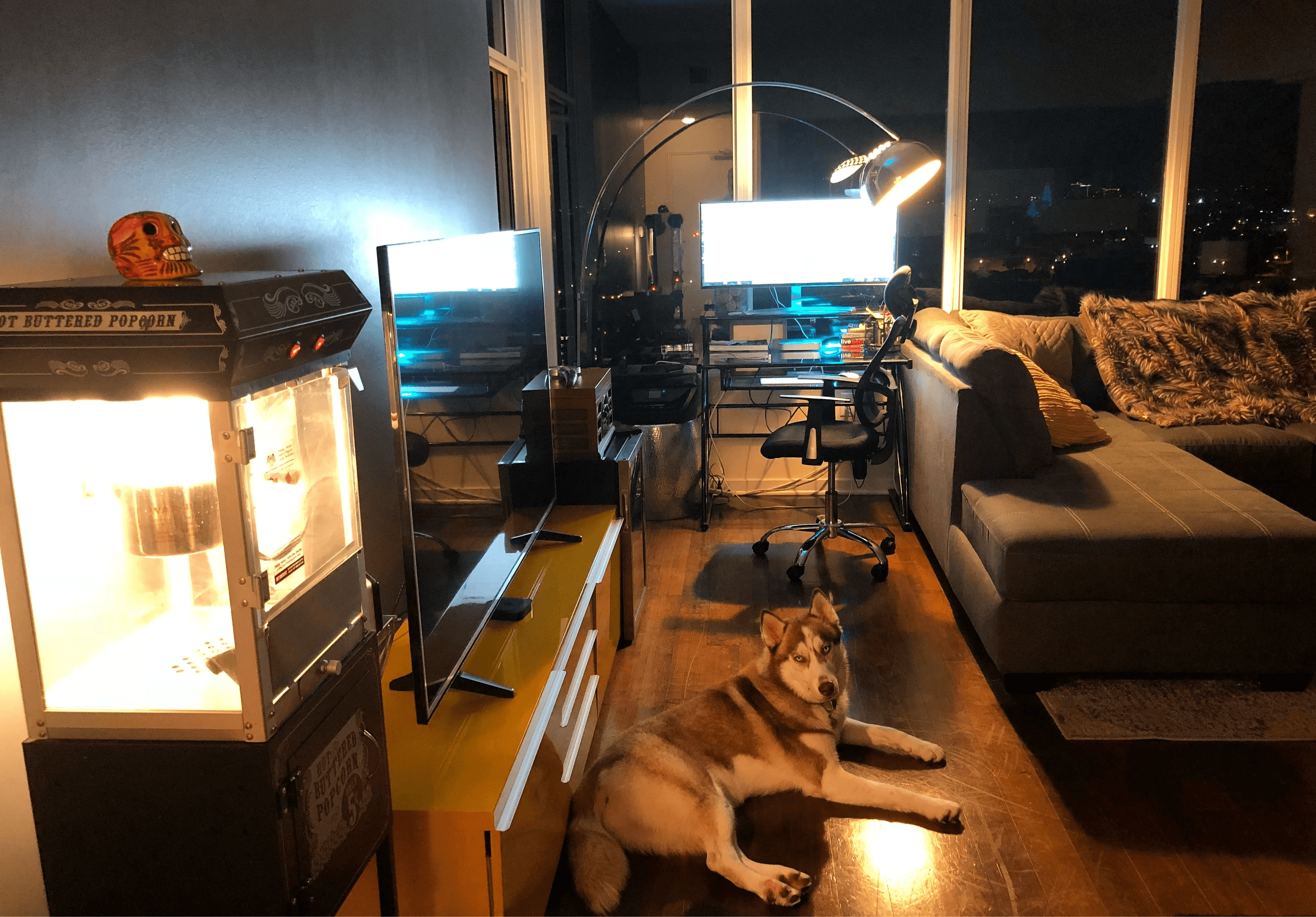 A cozy living room with a couch, computer setup, and a small illuminated display case. Warm, inviting atmosphere.
