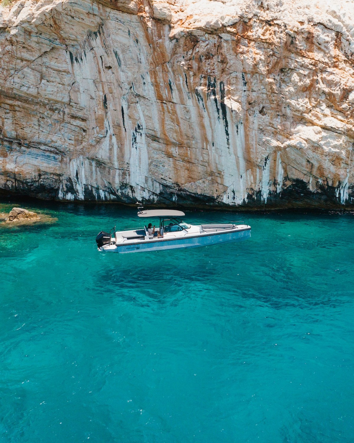 White Axopar 37 motor yacht anchored in turquoise waters near a dramatic sea cave with limestone cliffs.