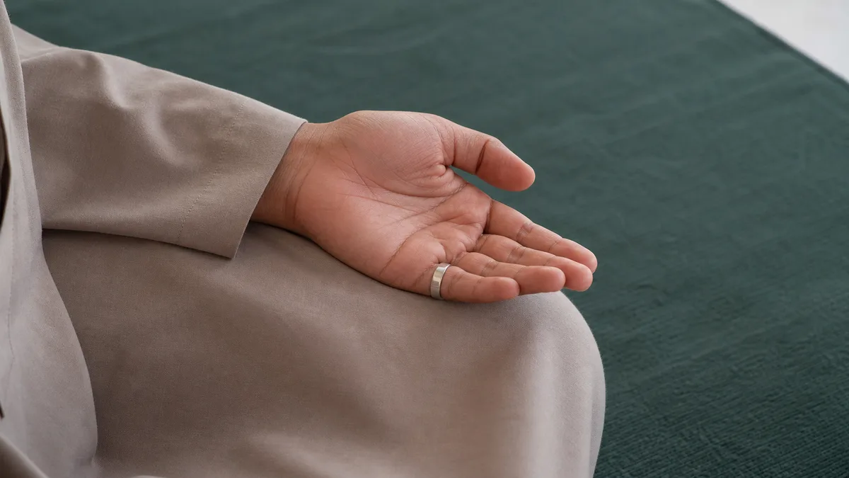 Open hand with a silver smart tasbih ring resting on the knee after salah for adhkar
