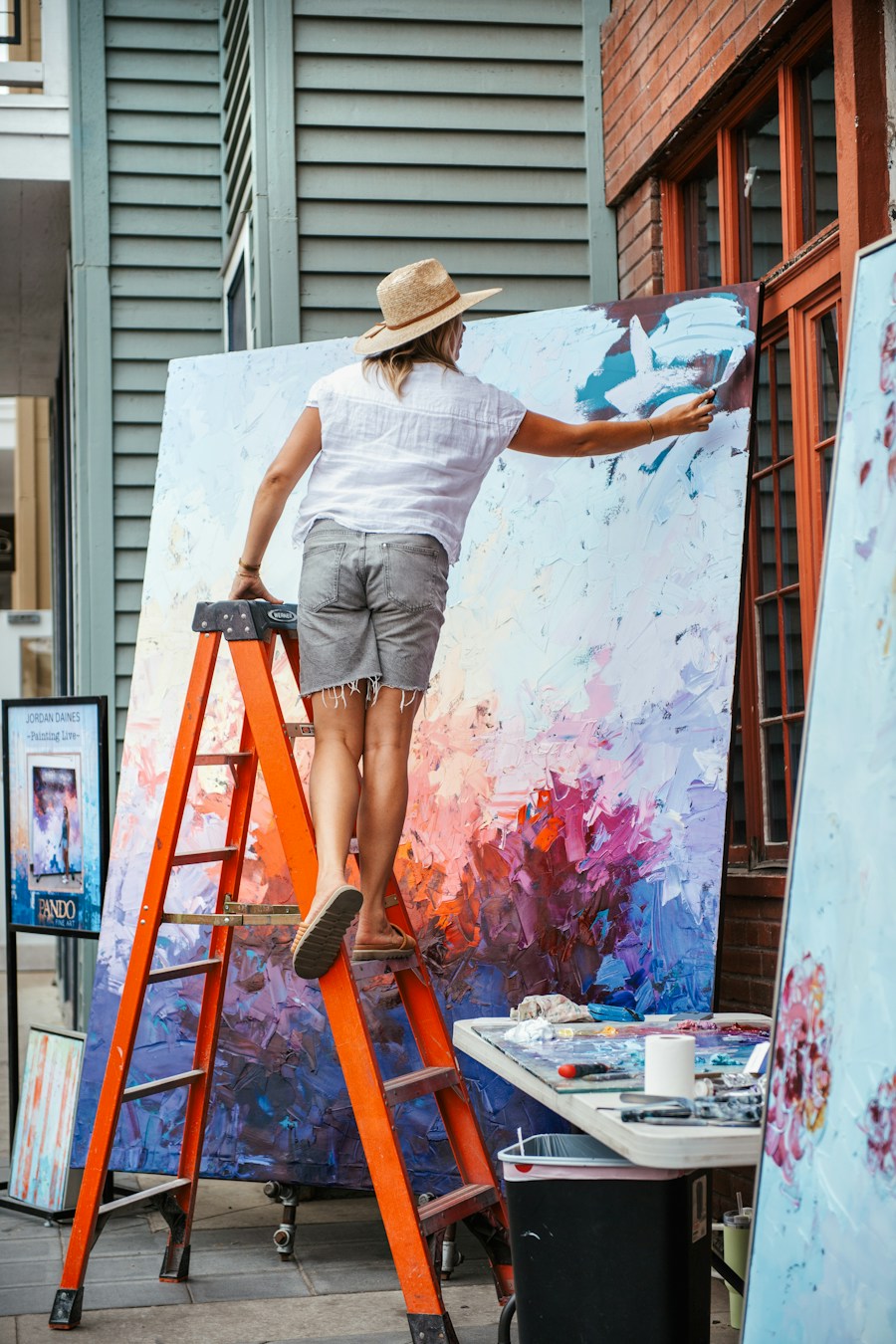 An artist reaching across a large, expressive abstract painting outdoors