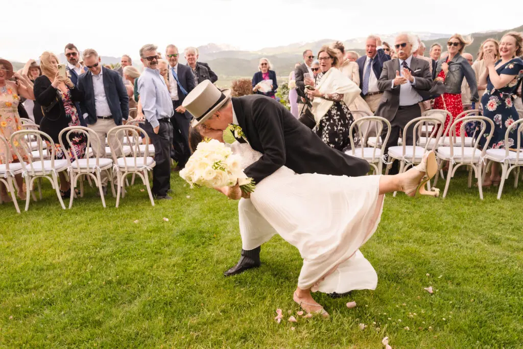 The groom playfully dipping the bride for a kiss on the ceremony lawn while guests cheer in the background at a Chaparral Ranch Wedding.