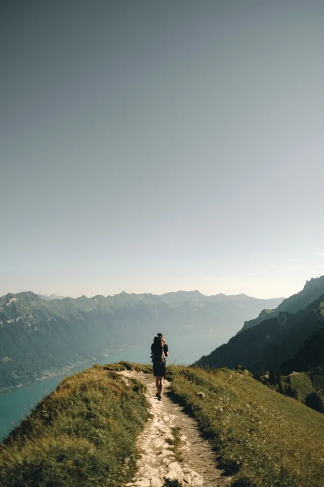Person standing on a narrow mountain trail above a lake