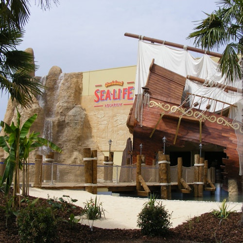 Eine Piratenschiffstruktur, die an einer felsigen Wand am Eingang des Sea Life Aquariums befestigt ist, umgeben von tropischen Pflanzen.