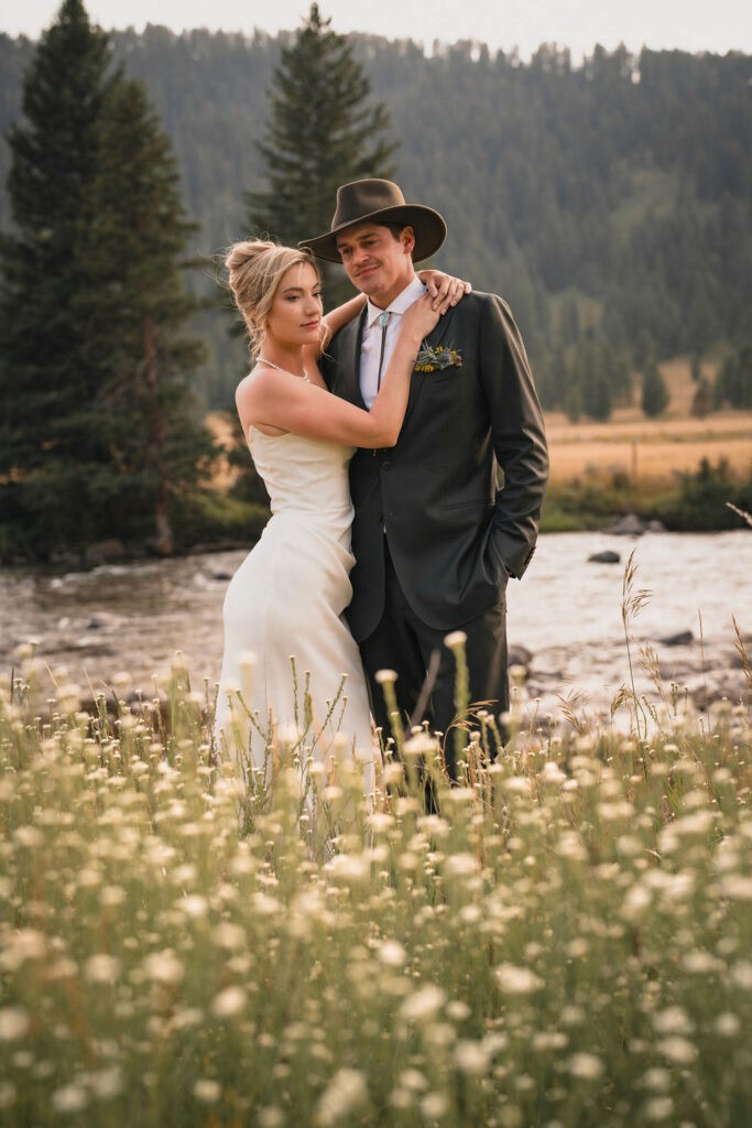 Newlyweds embracing among wildflowers near a river