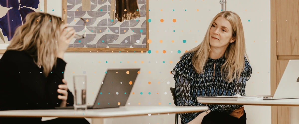 two team members sitting at their laptops disucssing across the tables