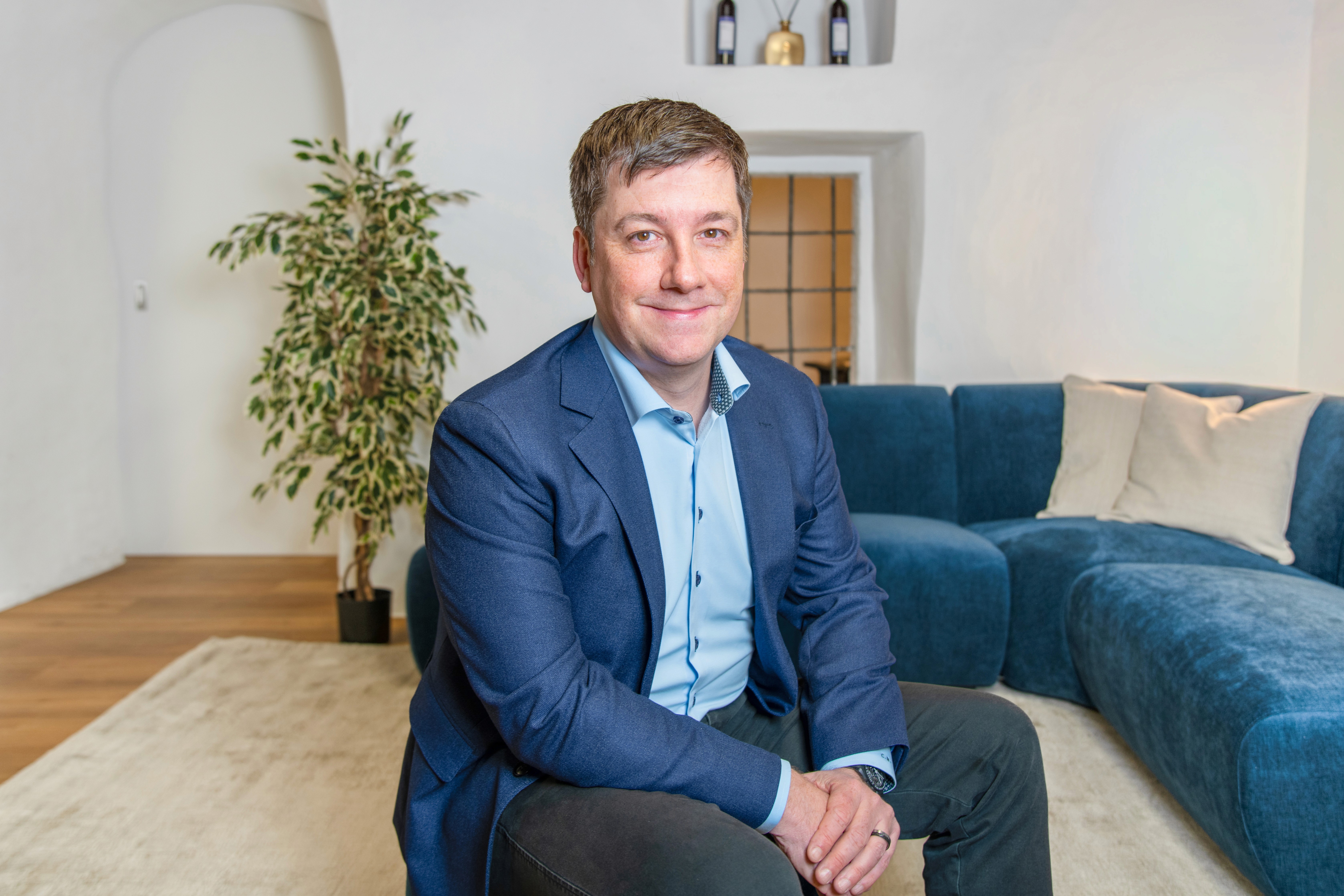 Immobilienmakler der Kocher Immobilien AG lächelnd vor einem blauen Sofa in der ImmoLounge