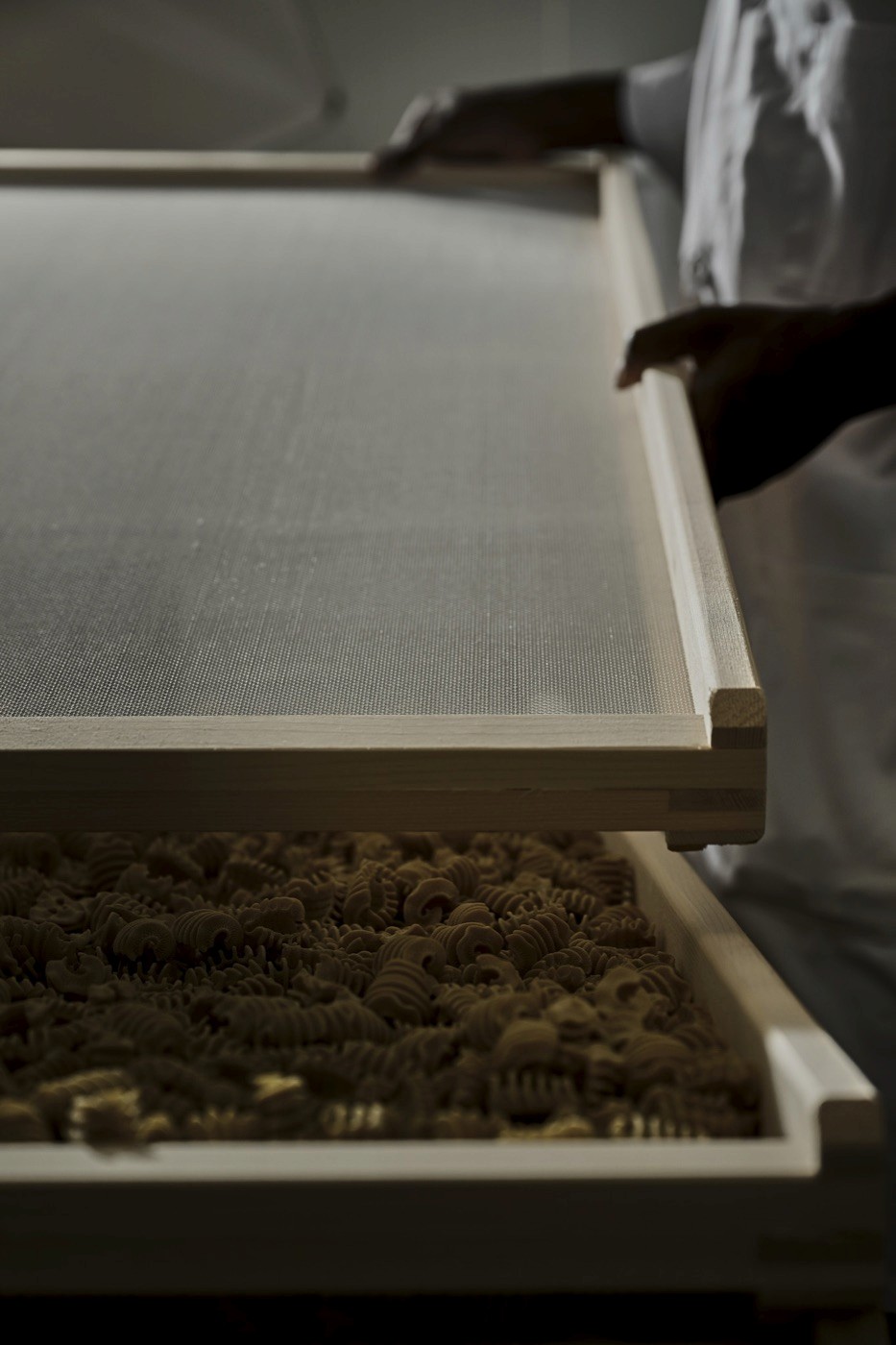 Hands lowering a mesh drying screen over a tray of spiral pasta.