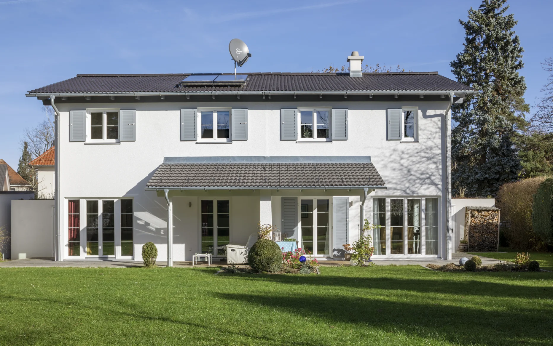 Ein modernes, freistehendes Haus mit weißer Fassade, Satteldach, Solaranlage und großer Rasenfläche bei Sonnenschein.