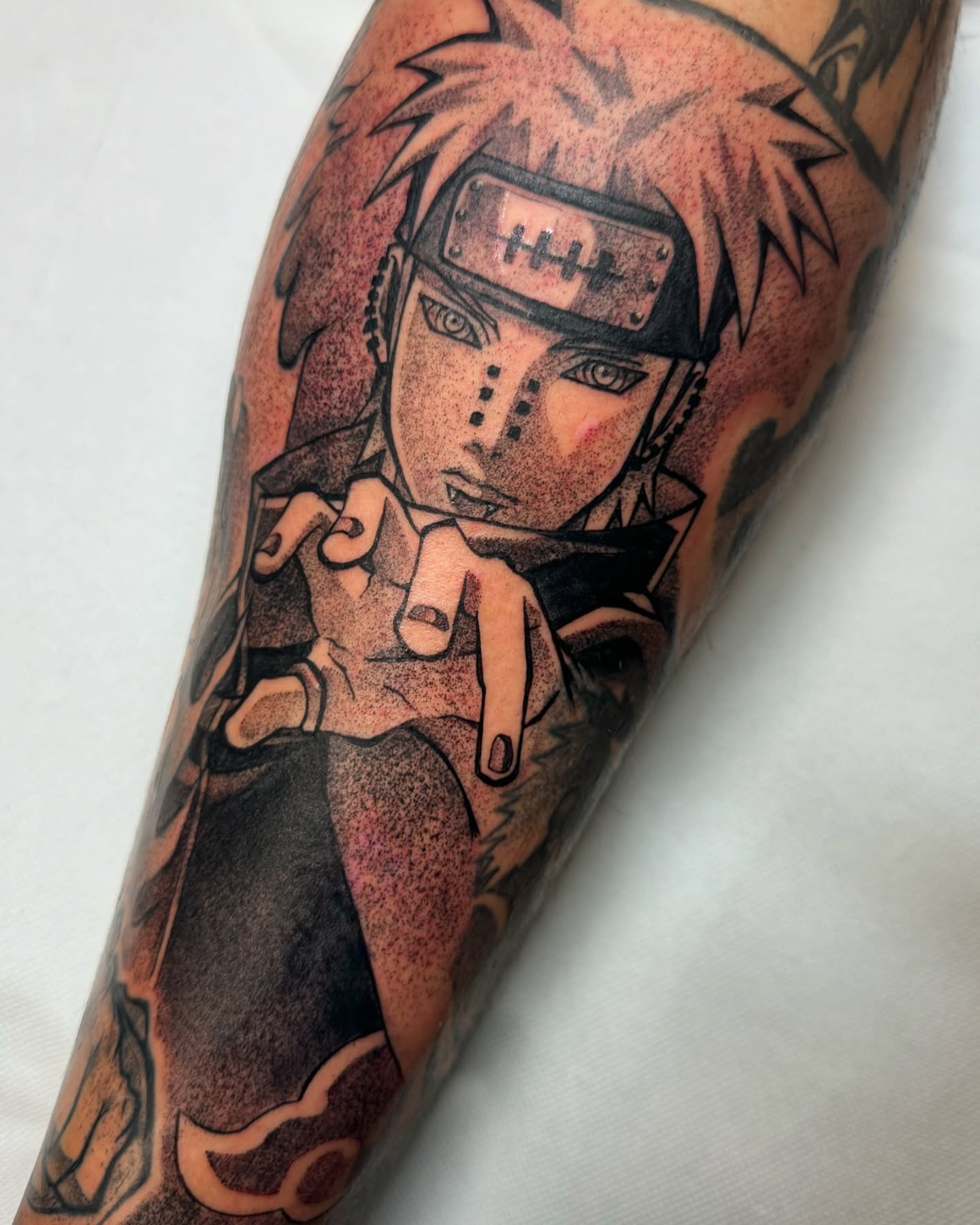 A grayscale anime-style tattoo of a character with spiky hair and a headband, holding a kunai.  The tattoo is on someone's forearm.