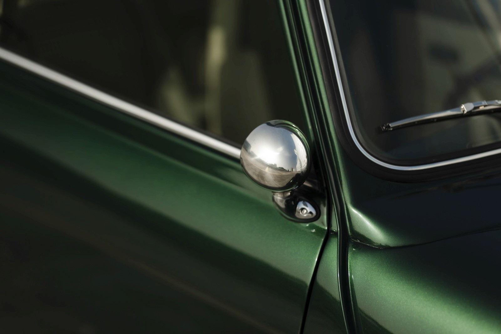 Close-up of a shiny side mirror on a vintage green car, showcasing the sleek design and chrome details.
