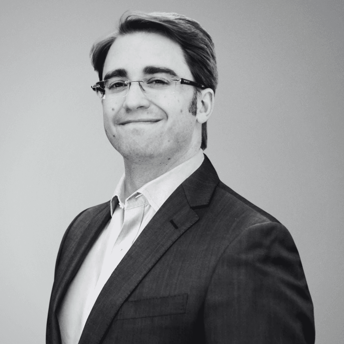 black and white photo of the upper part of a smiling man in a suit and white shirt without tie. This is the Chief Data Scientist of BeyondTrucks, Dr. John Carisson