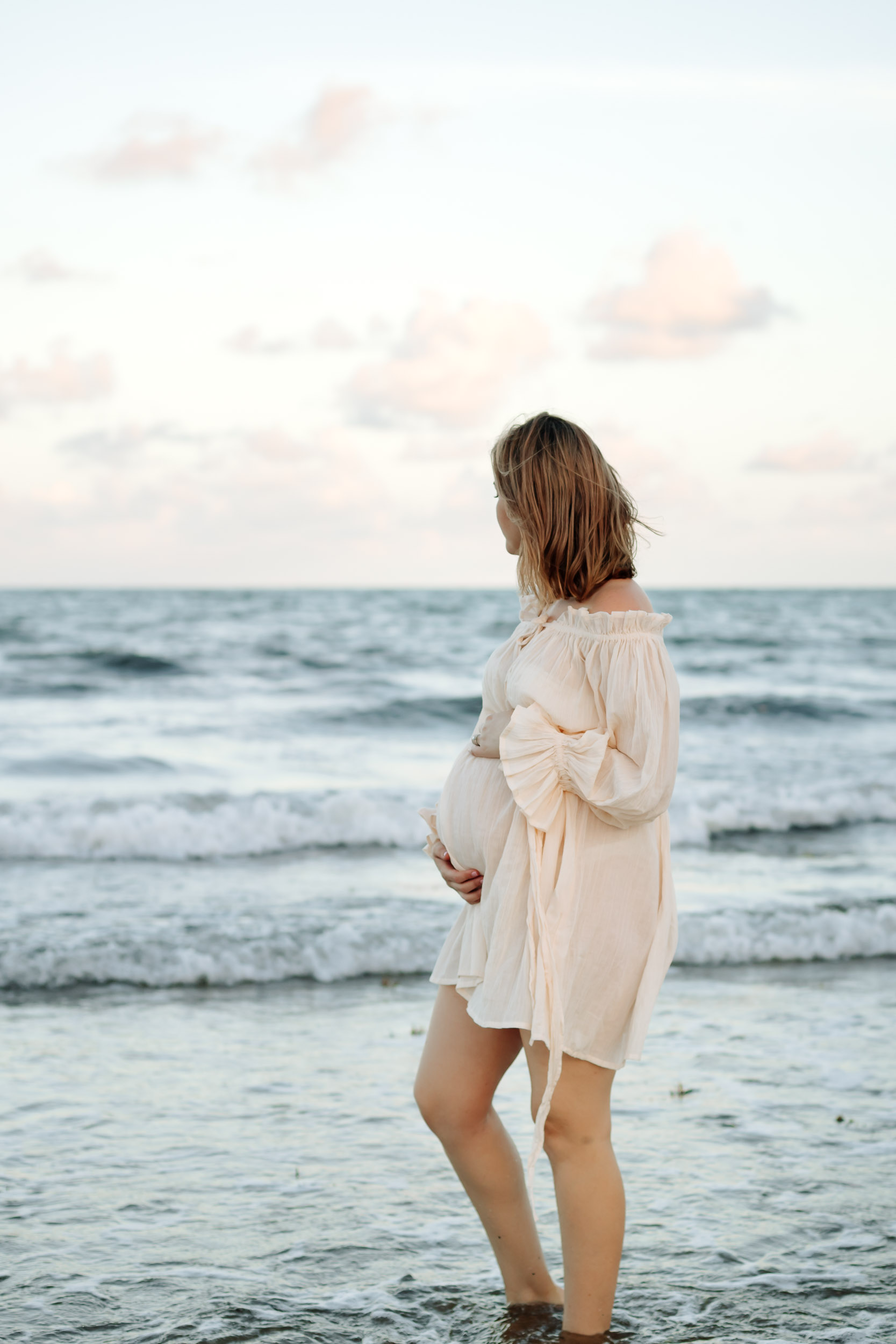 Solo maternity session on the beach at sunset in Mackay with expecting mother standing in soft golden light near the ocean.